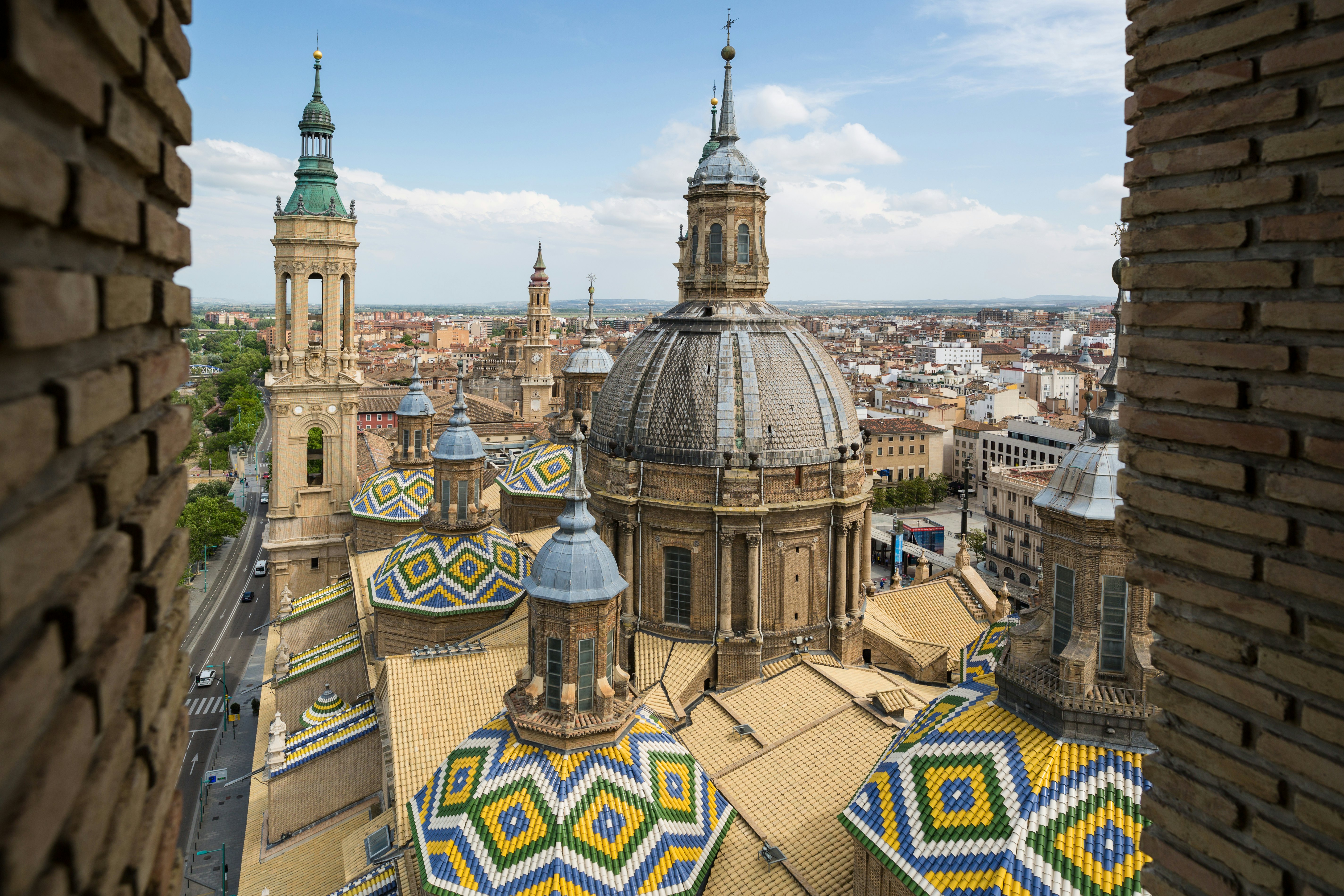 Roof and central dome of a vast cathedral building, with ornate tiled patterns, in the center of a city.