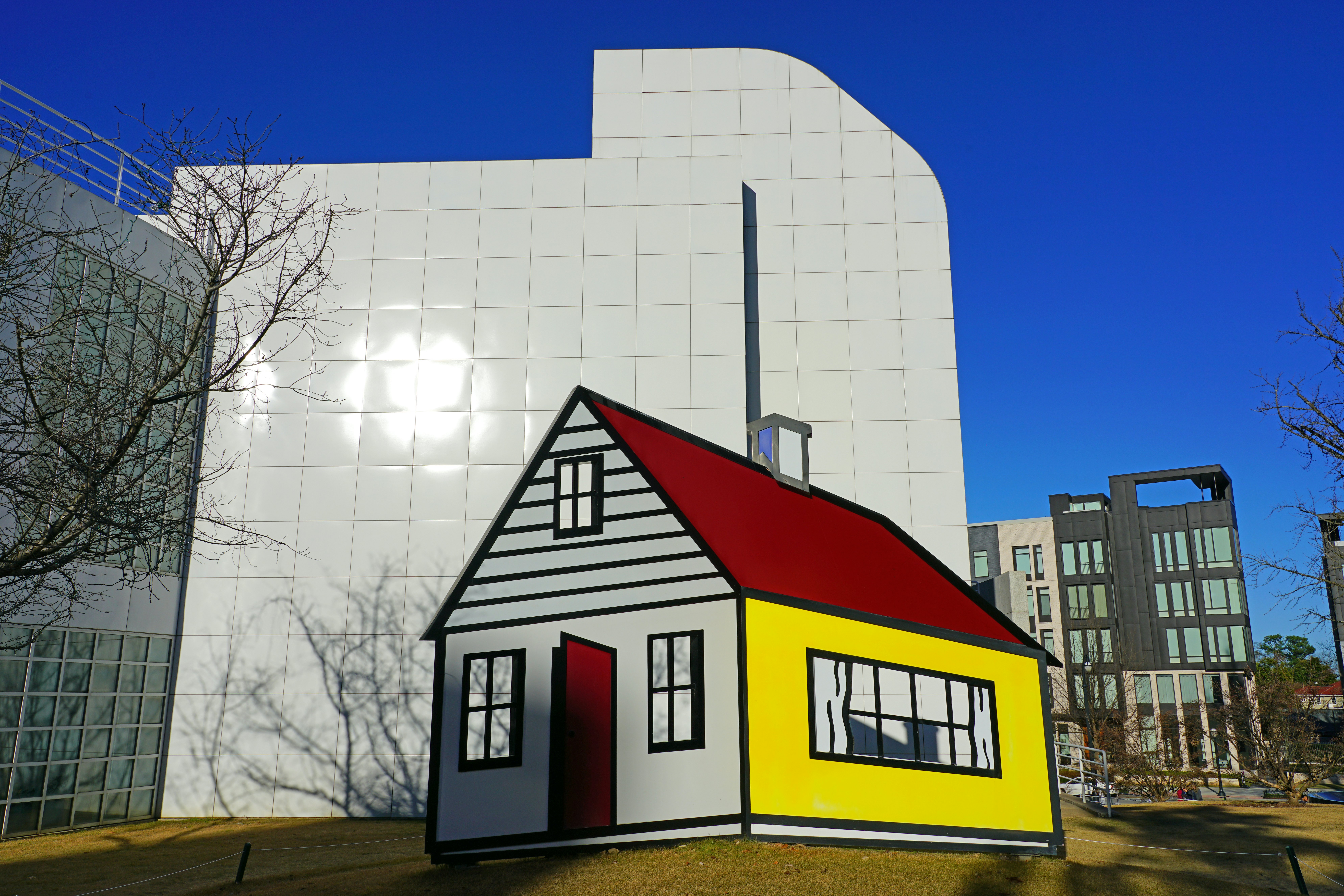 A sculpture depicts a house on the lawn in front of an art museum with a white facade.