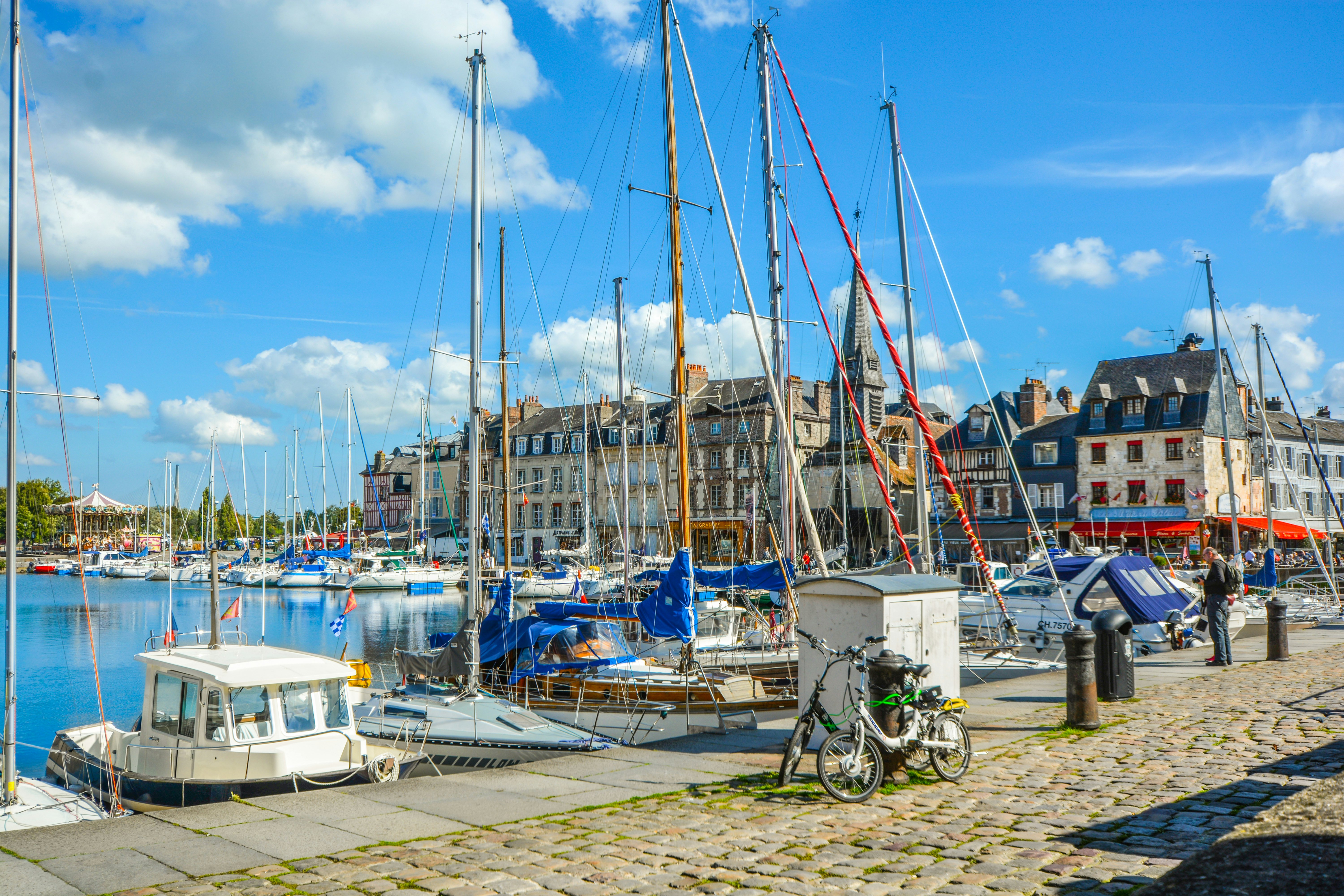 Two bikes lean agains a bollard on a cobbled street next to a harbor where many small boats are docked.