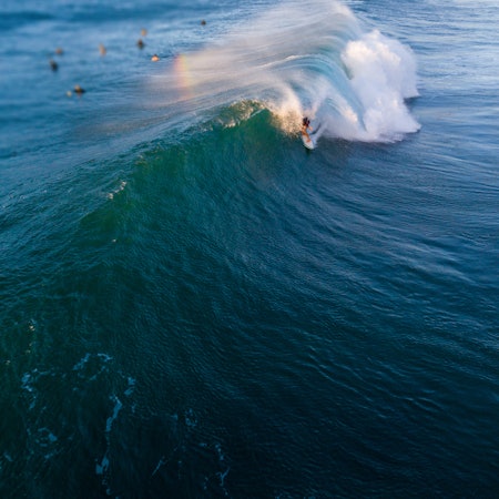 Surfer riding a large blue wave on a sunny day.