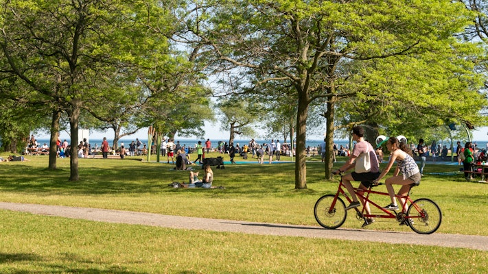 People riding a tandem bike through a busy green park