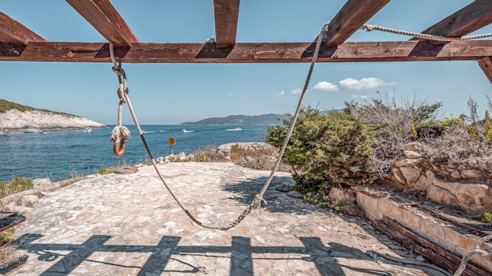 A rope swing on a stone patio overlooking a blue sea