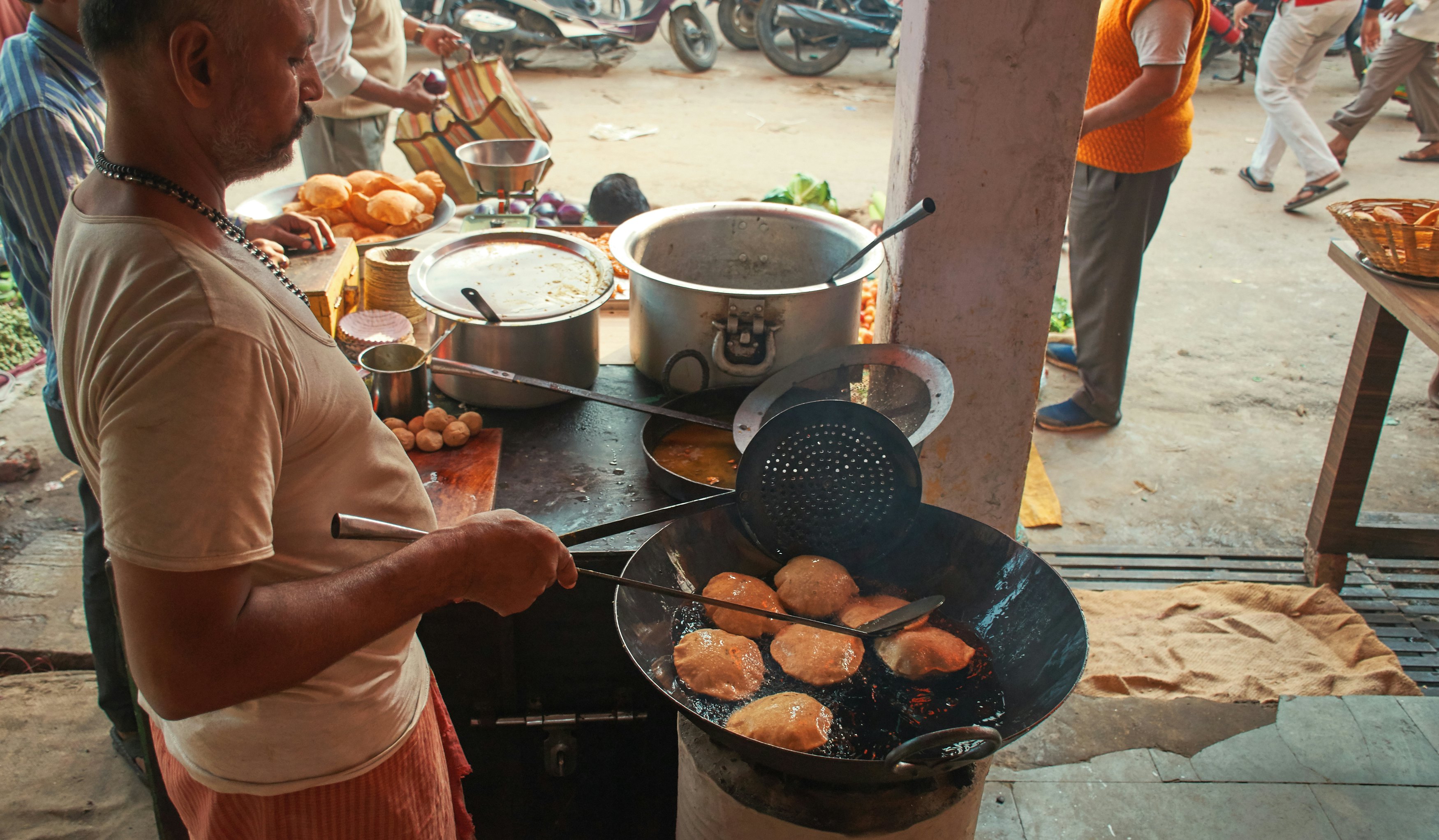 A man cooks a dish at a stall in a roadside stand in a city.