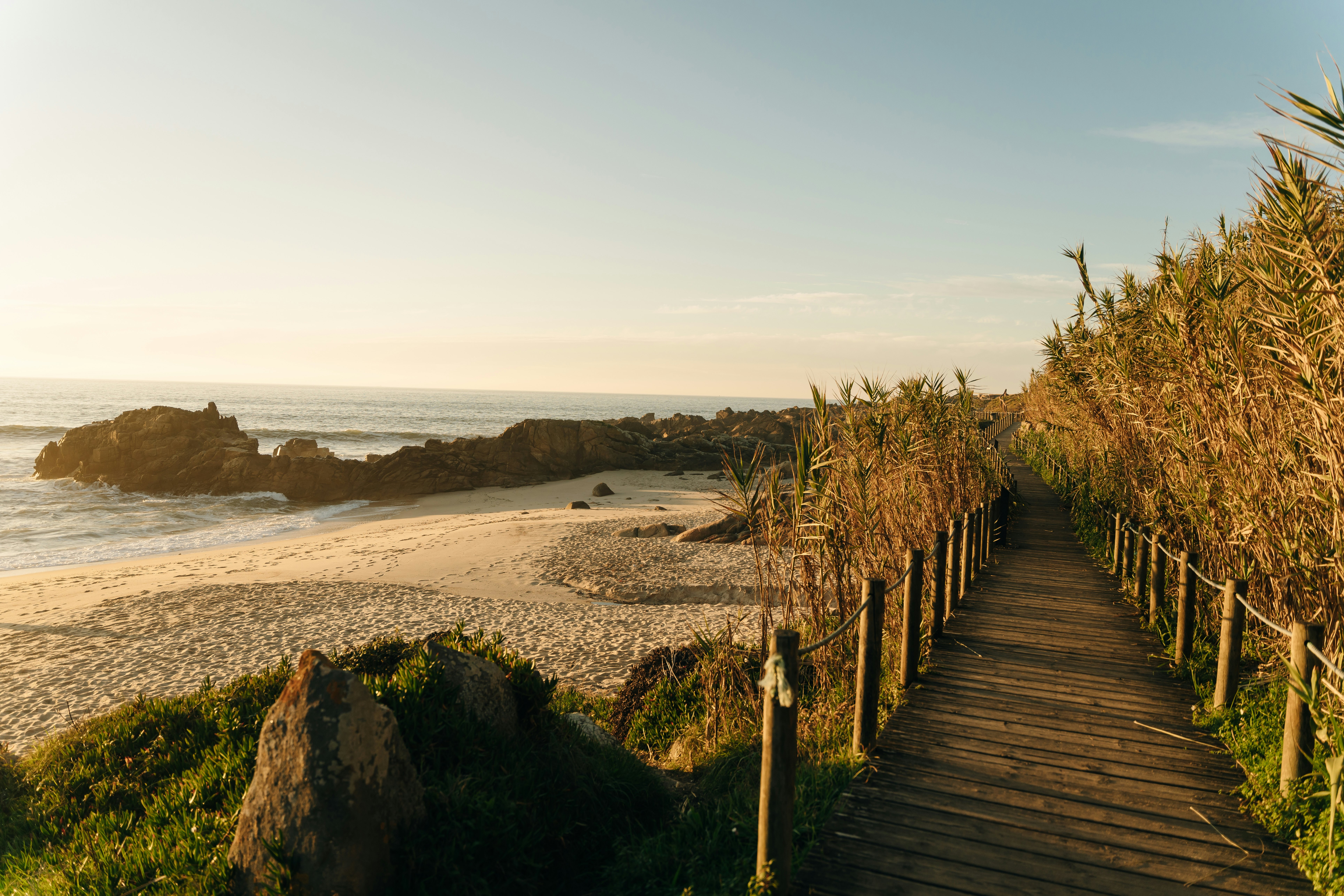 Sunny path alongside an empty beach looking out to rocks in the sea