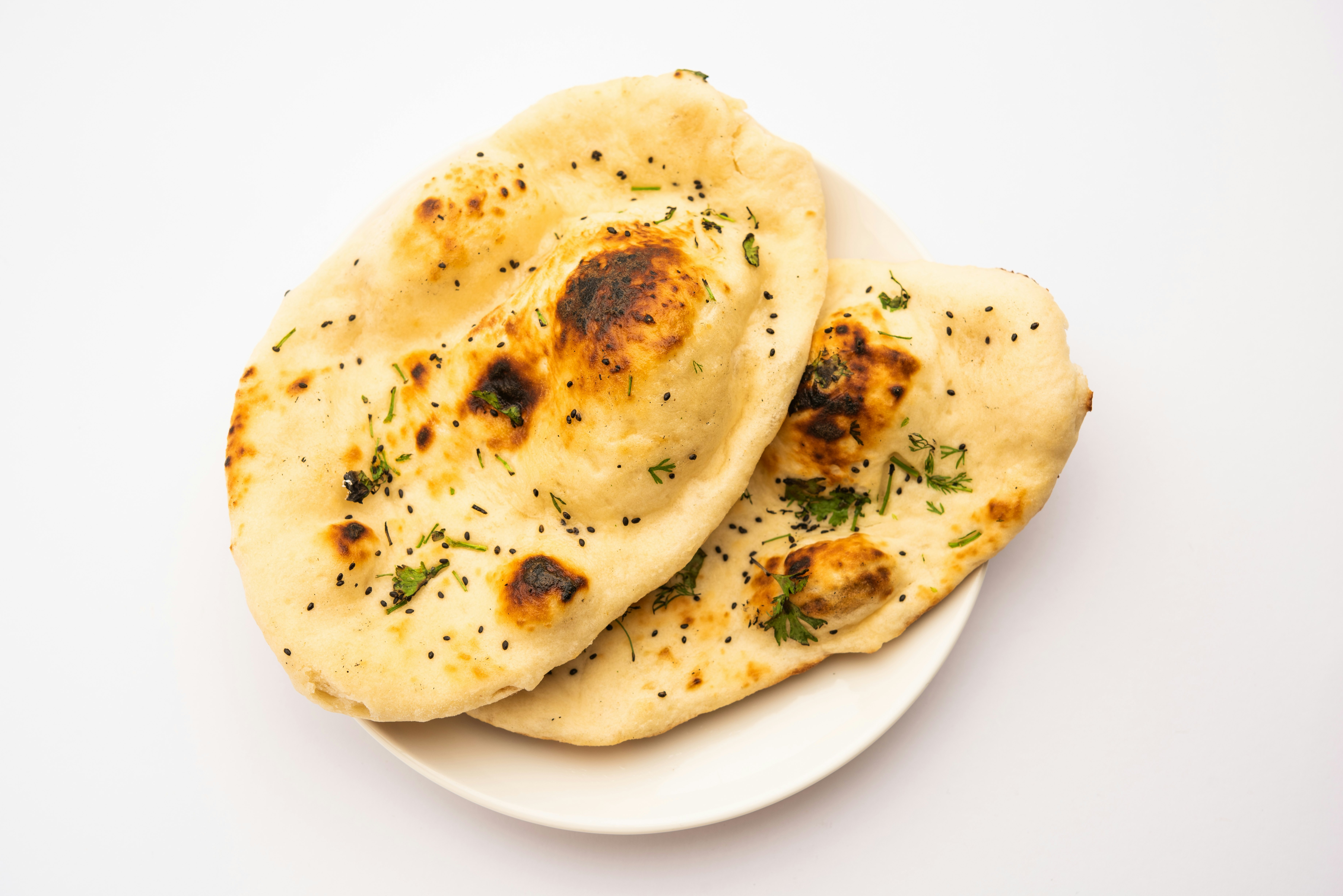Two pieces of naan bread flecked with green and brown spices, resting on a white plate