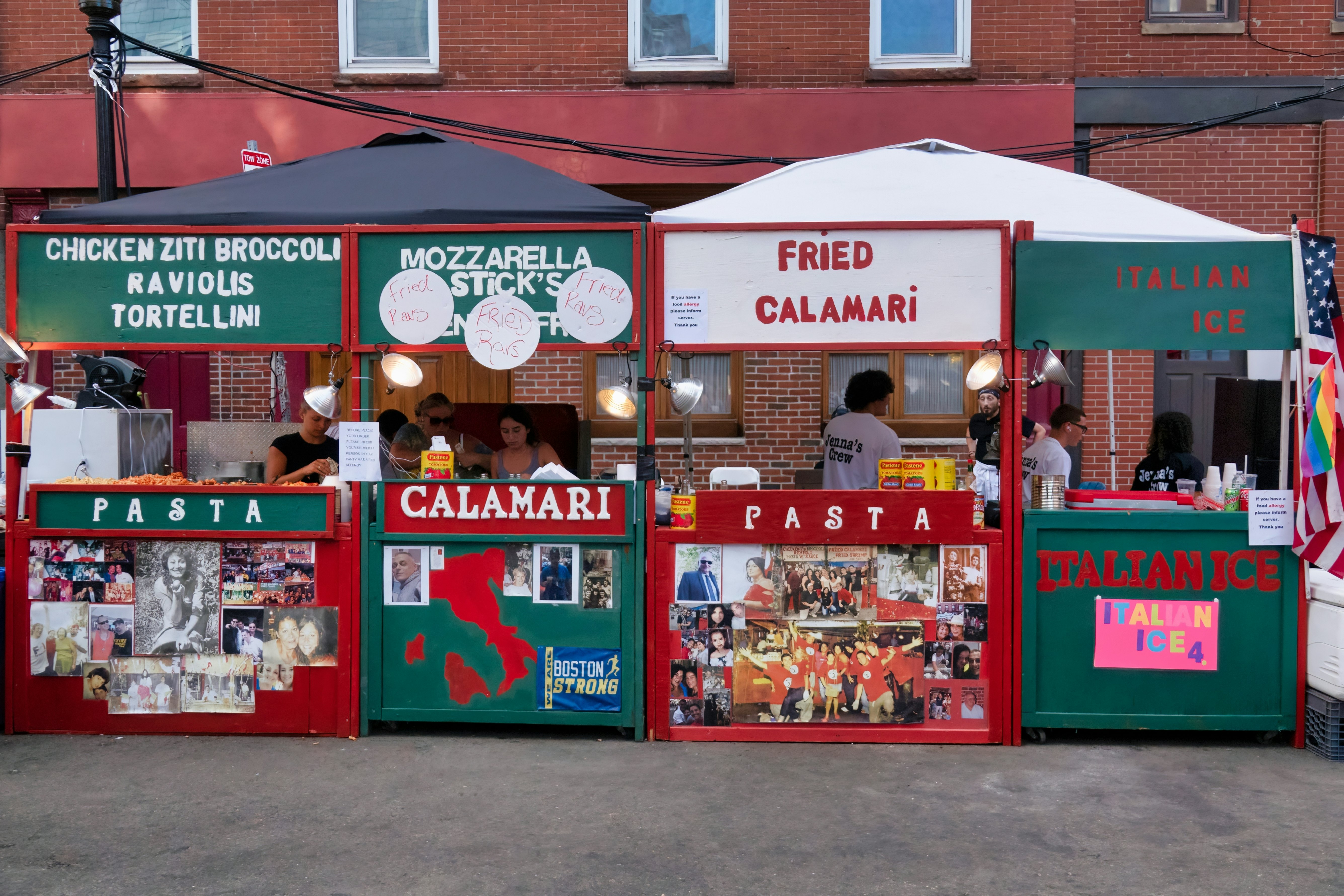 Red and green booths with vendors selling Italian food are set up on a city street.
