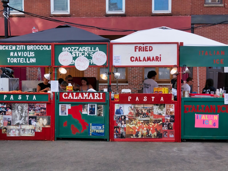 Wooden stands painted green and red with words like, fried calamari, mozzarella sticks and pasta. People are behind the stands