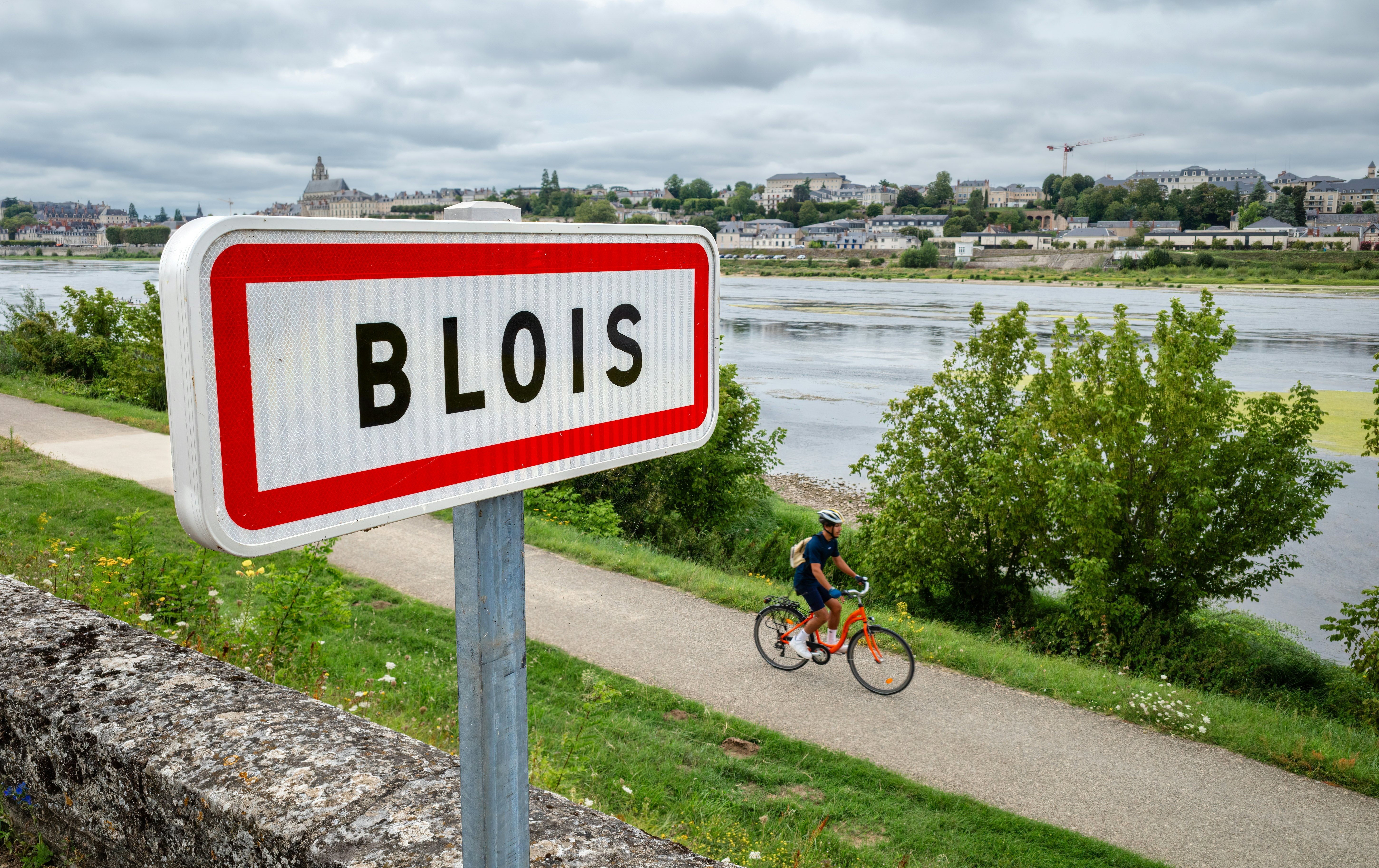 A cyclist on a towpath beside a wide river. A nearby sign reads "Blois".