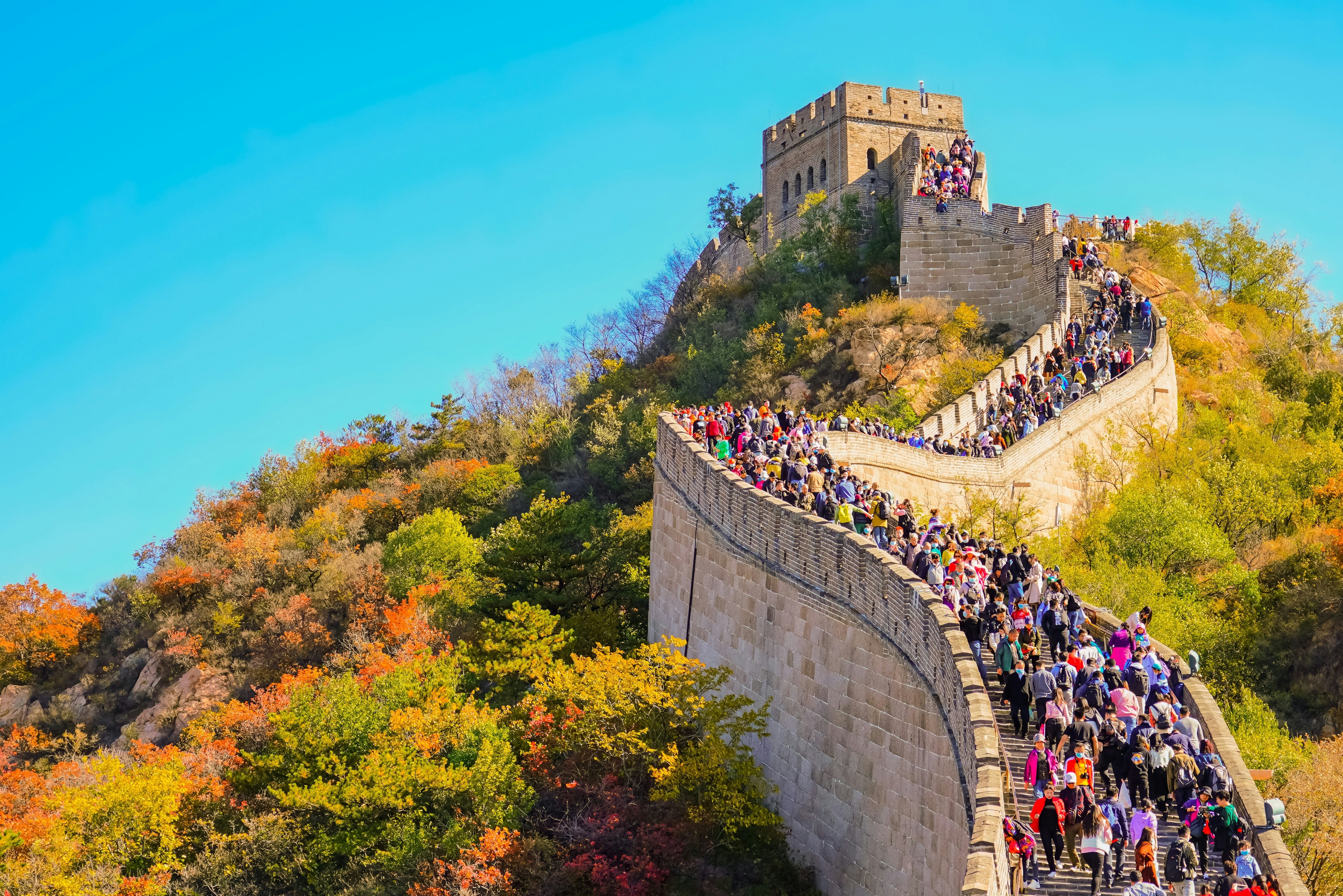 Crowds of people walk along the ramparts of a vast wall on a sunny autumn day.