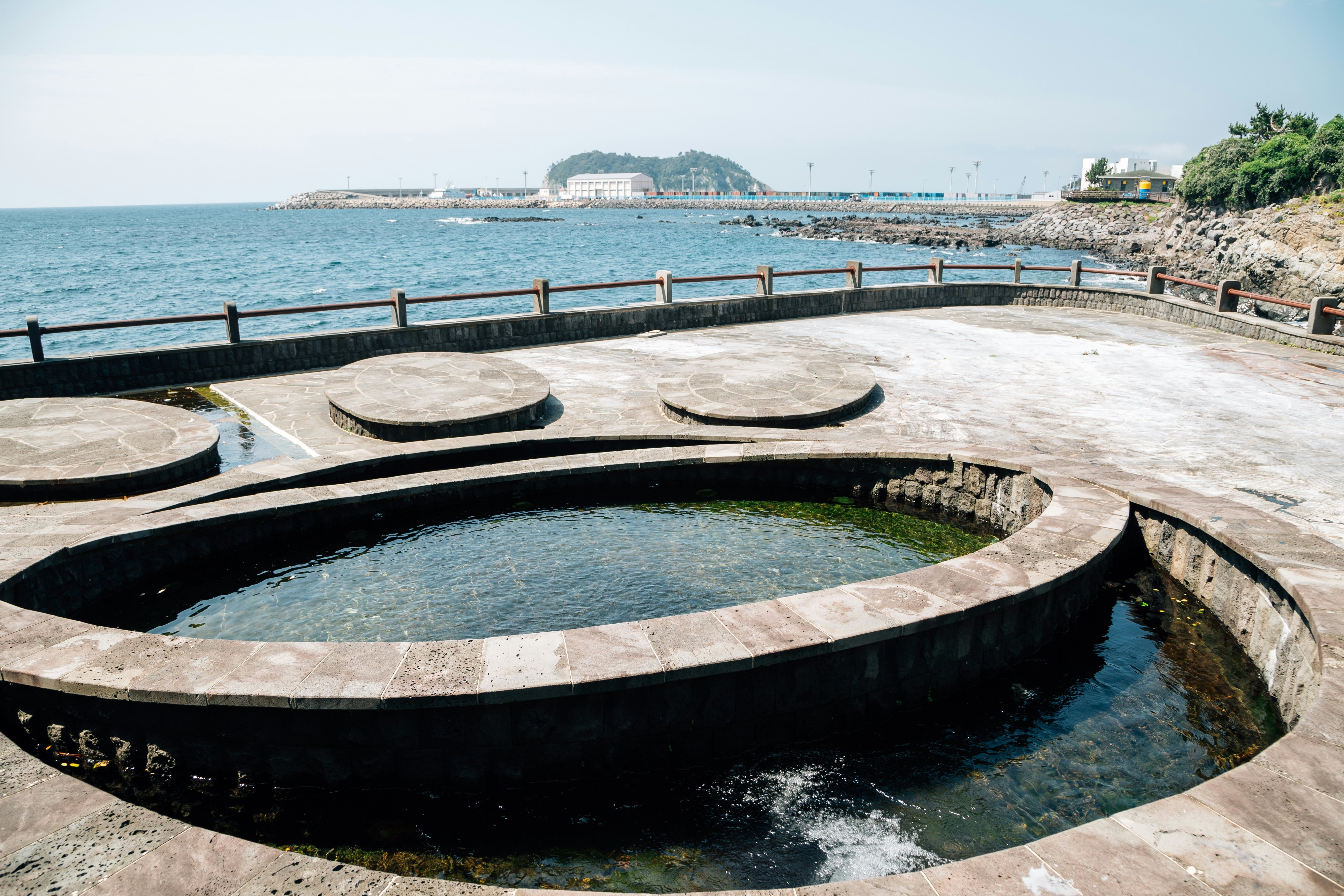 An outdoor public bath of two concrete pools full of spring water facing the ocean.