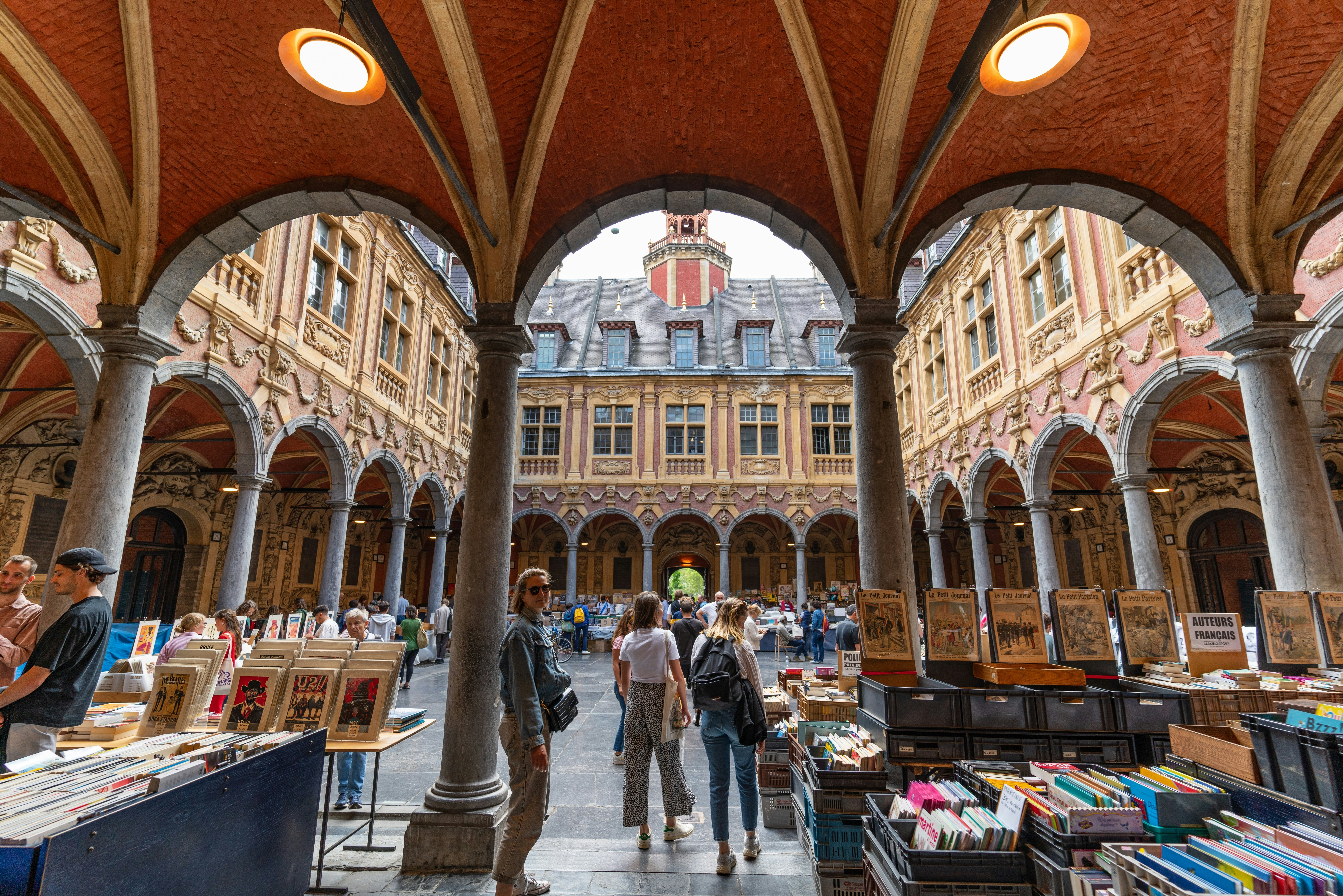 Shoppers and browsers wander around a secondhand book market within the covered arcade of a former stock exchange.