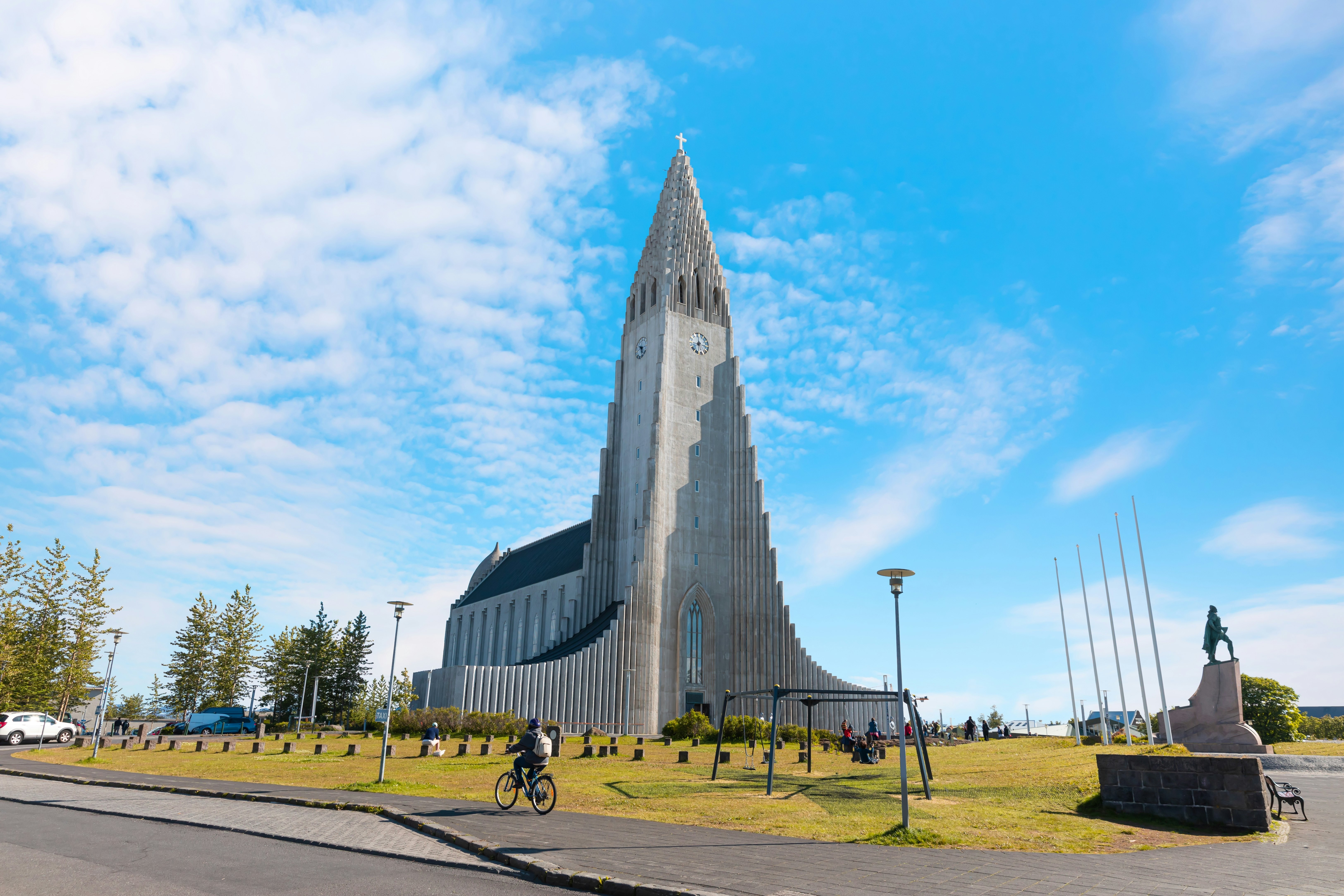 Hallgrímskirkja Lutheran parish church on a sunny day with trees, grass and a cyclist in the foreground