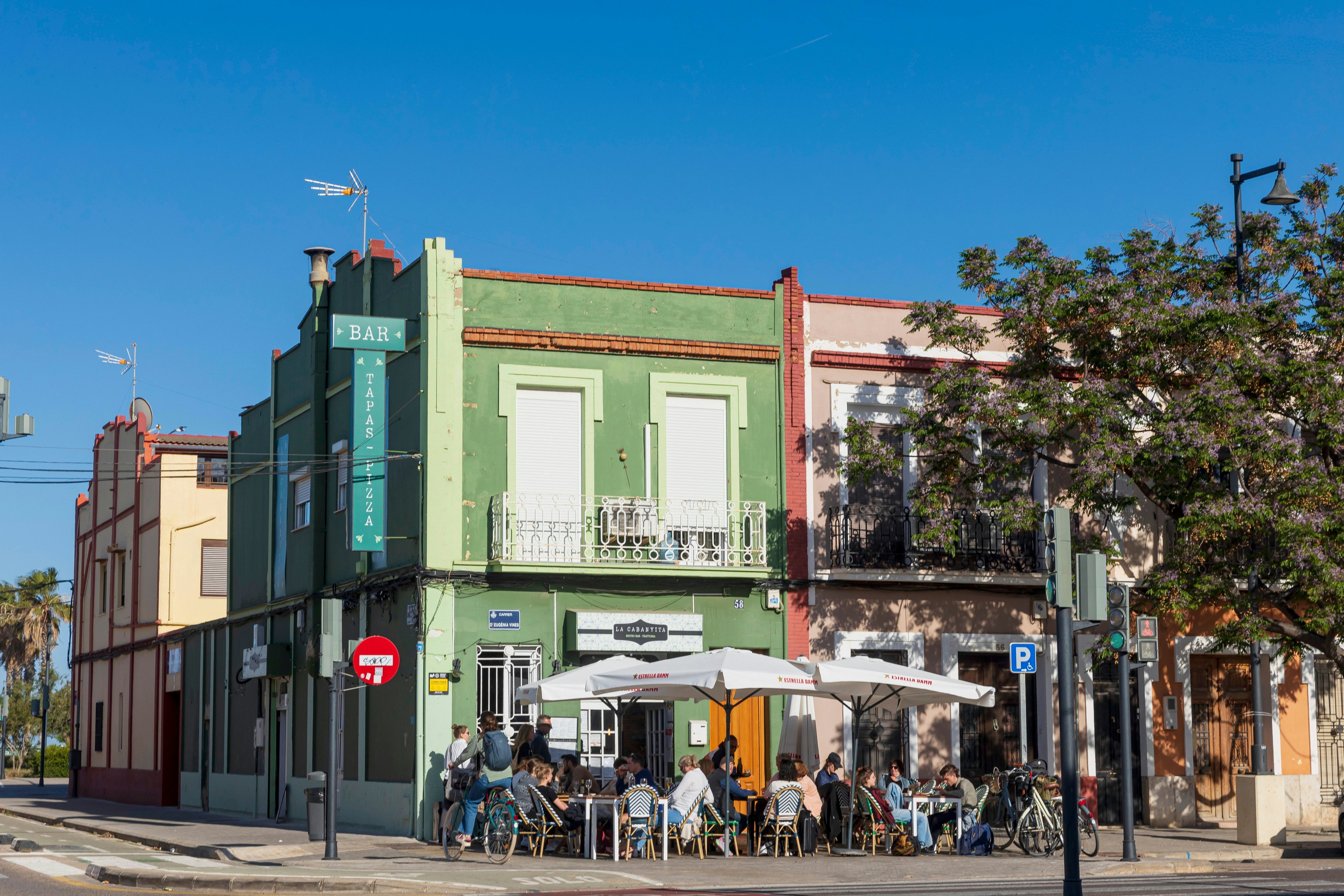People sit at outdoor tables in front of a restaurant in a green building.