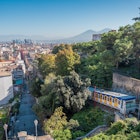 Funicular riding from the lower part of the napoli city towards the saint elmo fortress above the ground. Visible panorama of the napoli city with the white and blue funicular, License Type: media, Download Time: 2025-06-17T11:00:10.000Z, User: clairenaylor, Editorial: false, purchase_order: 65050 - Digital Destinations and Articles, job: Online editorial, client: Naples getting around, other: Claire Naylor