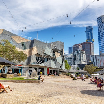 Melbourne, Australia - 21 January 2023: People enjoy the summer weather in Federation Square, Melbourne, Australia. The modern cultural centre is a hub for the arts, and is lively with bars and cafes., License Type: media, Download Time: 2025-06-29T19:35:43.000Z, User: LP_KBaxter, Editorial: true, purchase_order: 65050 - Digital Destinations and Articles, job: Lonely Planet, client: Melbourne v Sydney, other: Kathleen Baxter