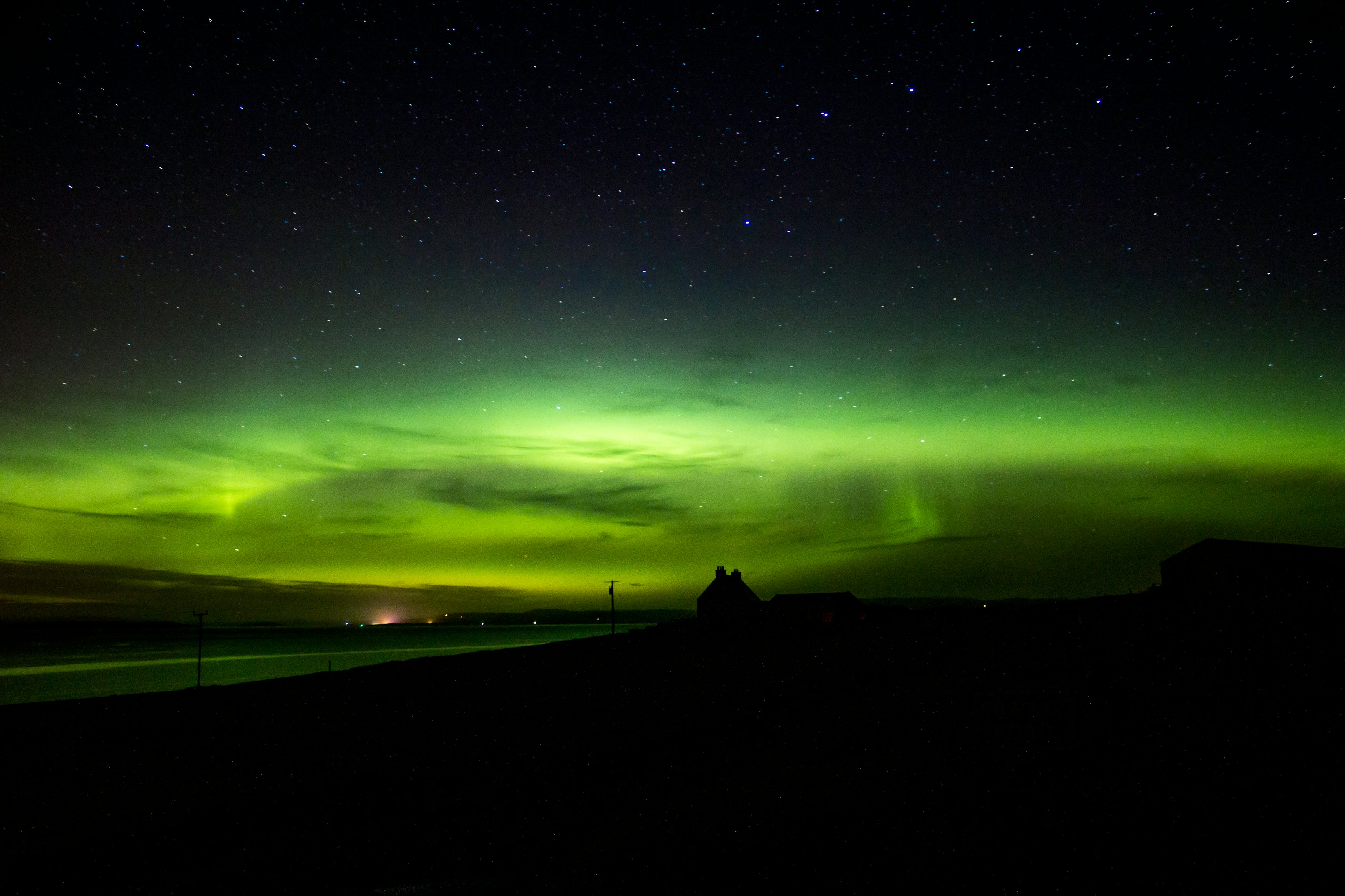 Green lights from the aurora borealis in a dark sky with a building silhouetted in front.