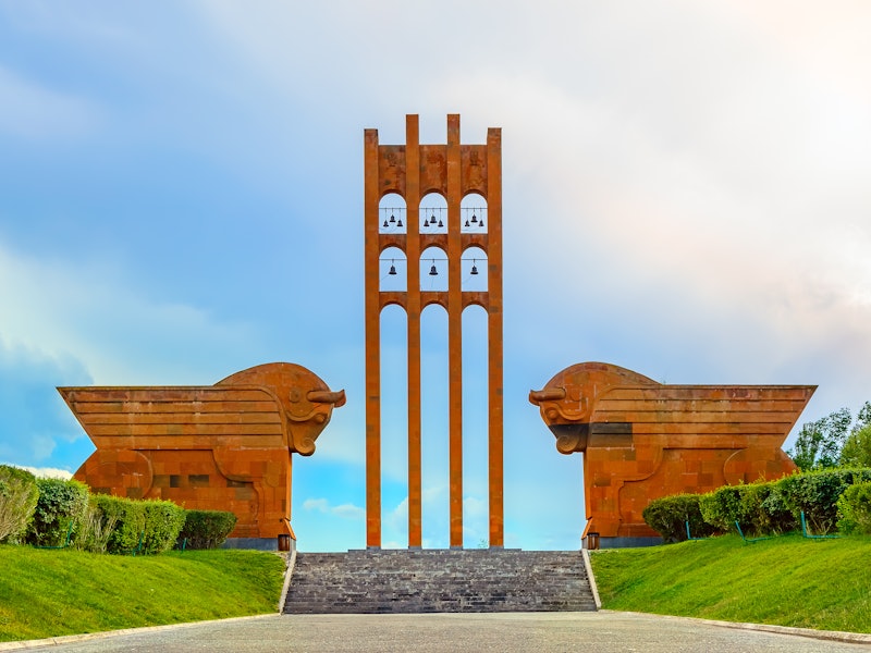 Two large orange bulls flank the staired entrance of a memorial that has an orange tower with bells
