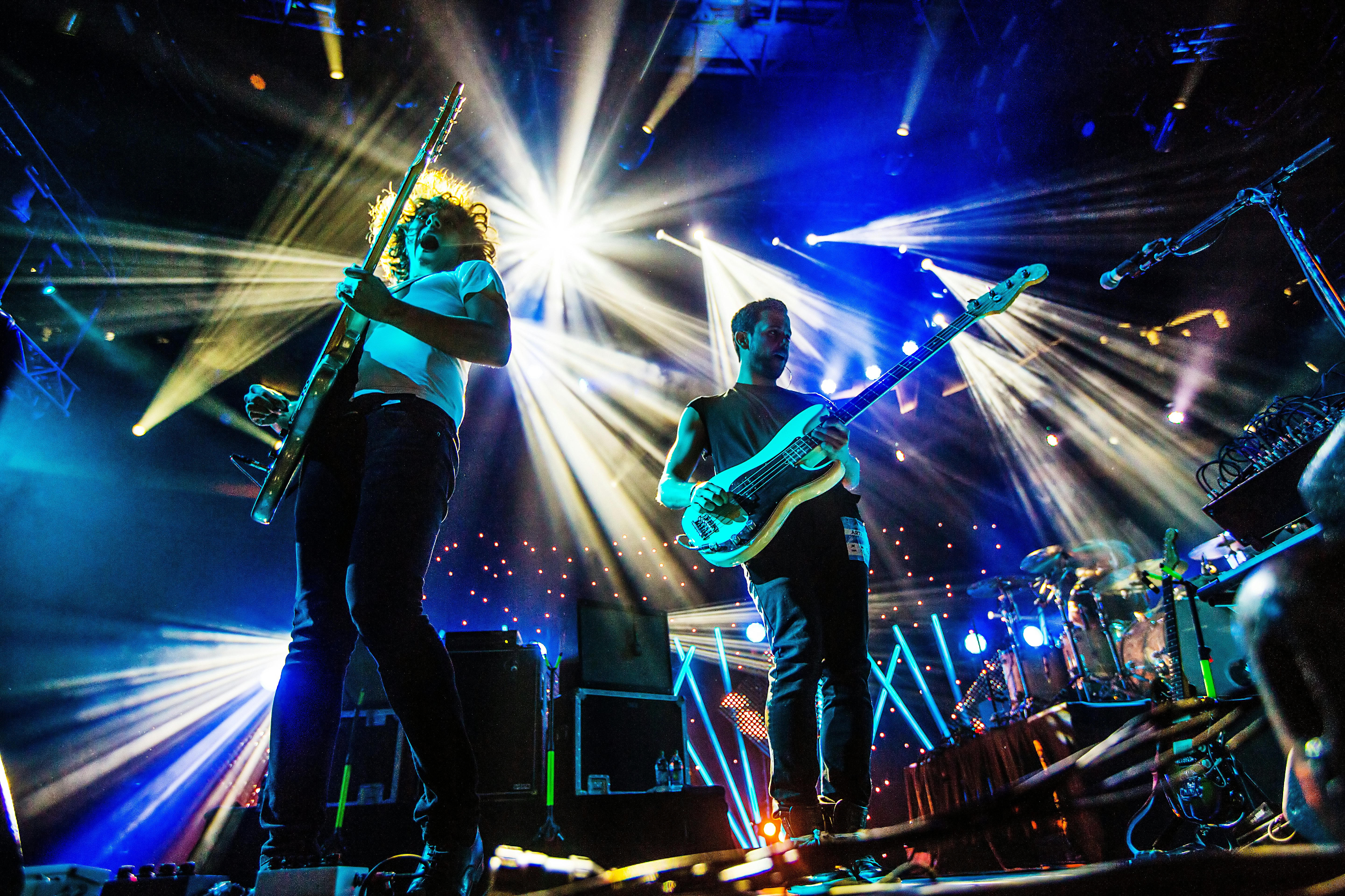 Two guitarists onstage with bright lights streaming down behind them during a concert