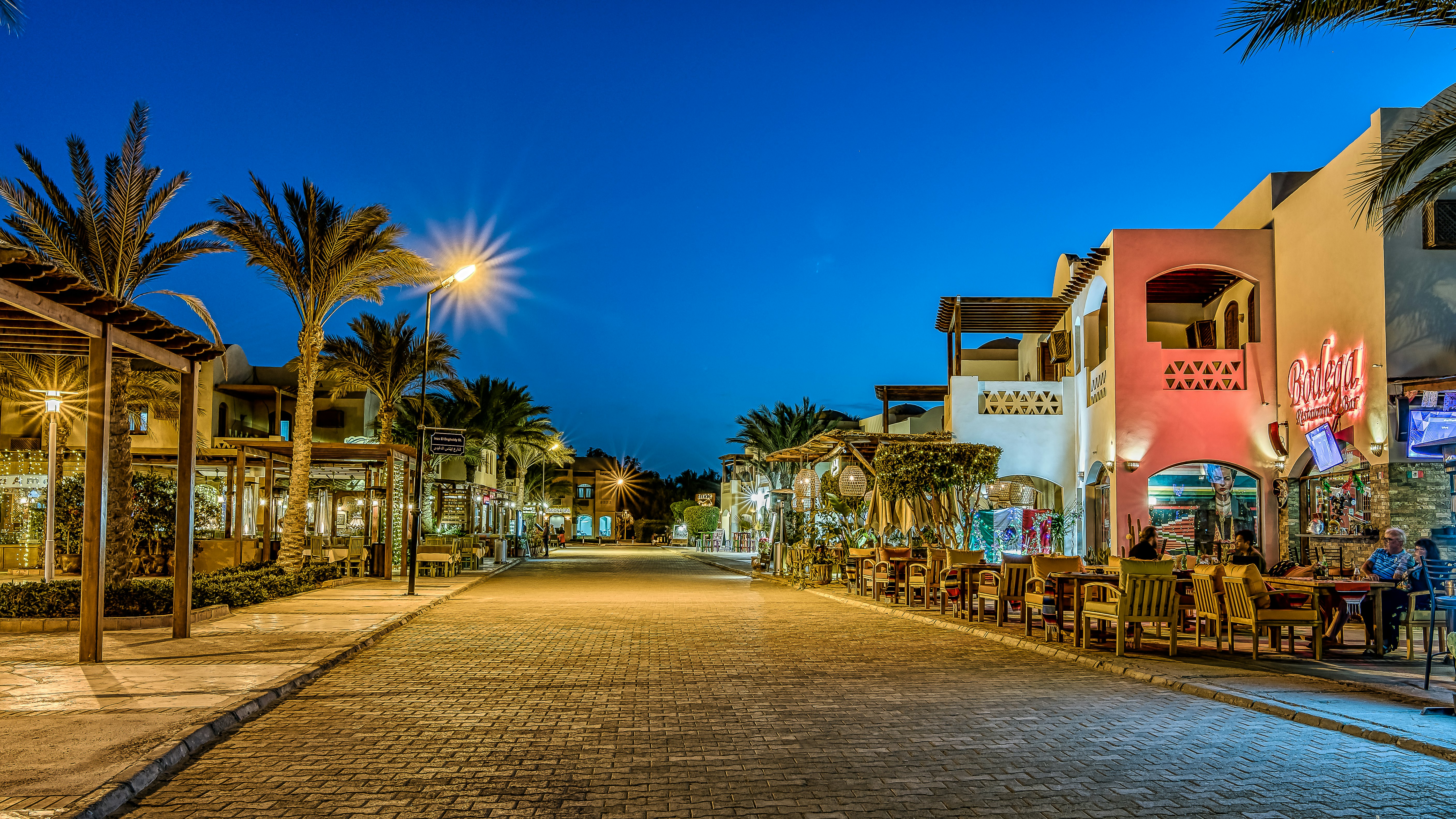 Nighttime view of a street lined with restaurants, shops and palm trees