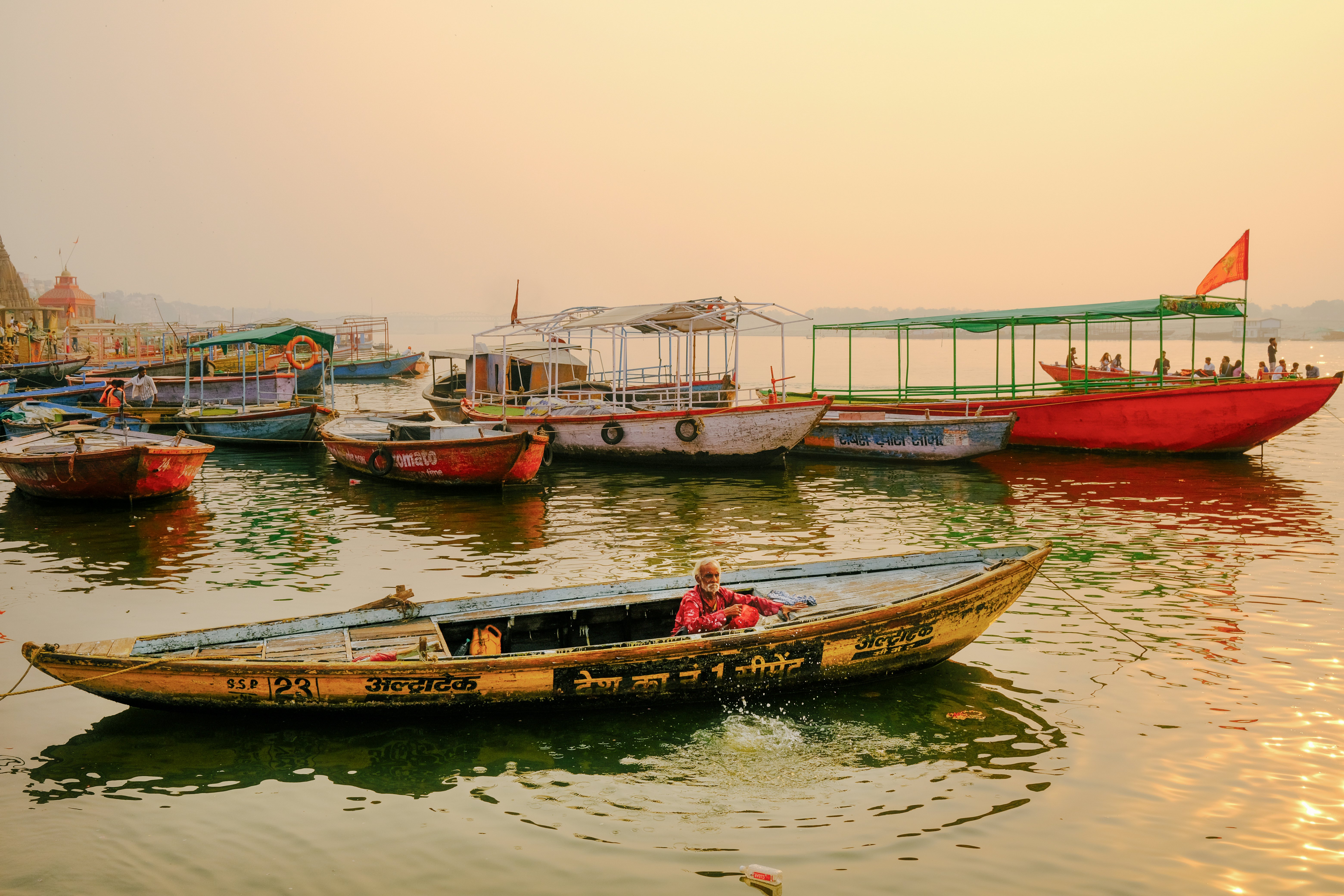 A man in his small wooden boat on a river at sunrise.
