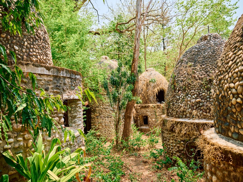 Stone buildings built close together with round stone and thatch roofs in a forested area.