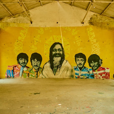 A yellow wall painted with an image of the band The Beatles surrounding famed Maharishi Mahesh Yogi
