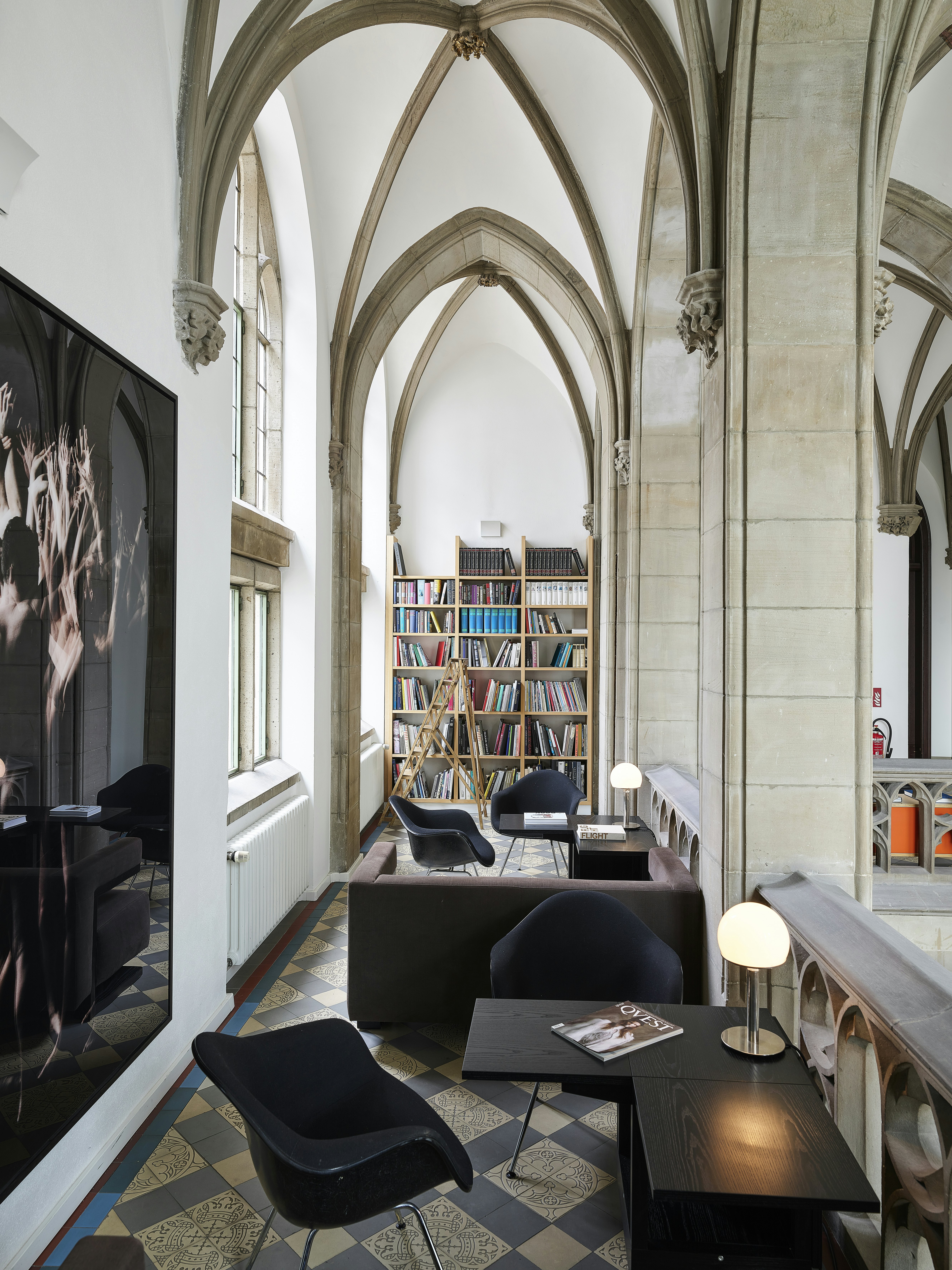 A stylish reading space on a mezzanine, with sofas, chairs, low lighting and a bookshelf at the end.