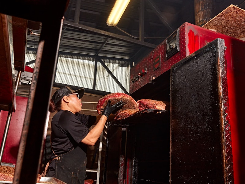 A cook adds brisket to an enormous oven