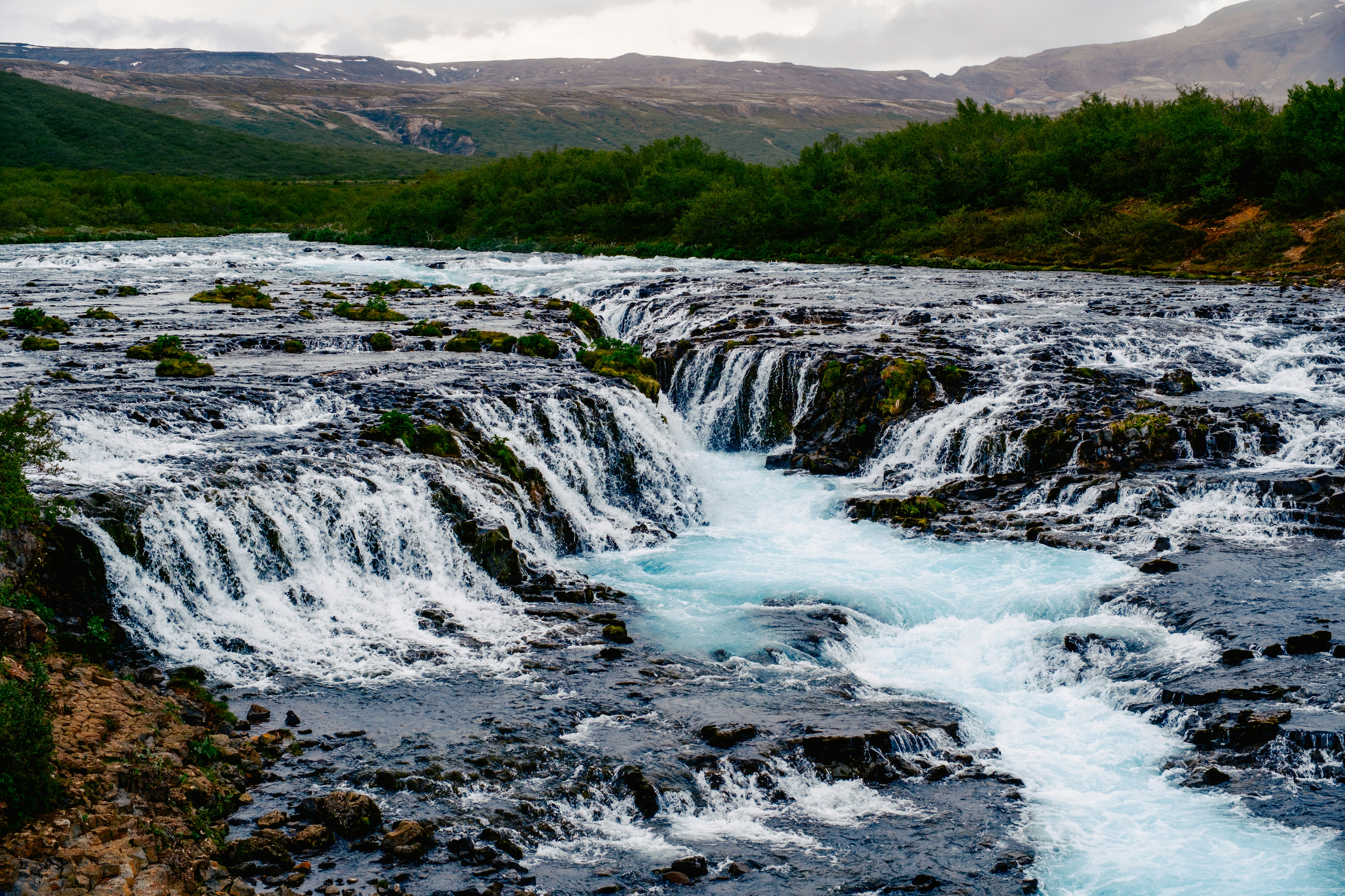 Rapids tumble over rocks along a river in a misty landscape.