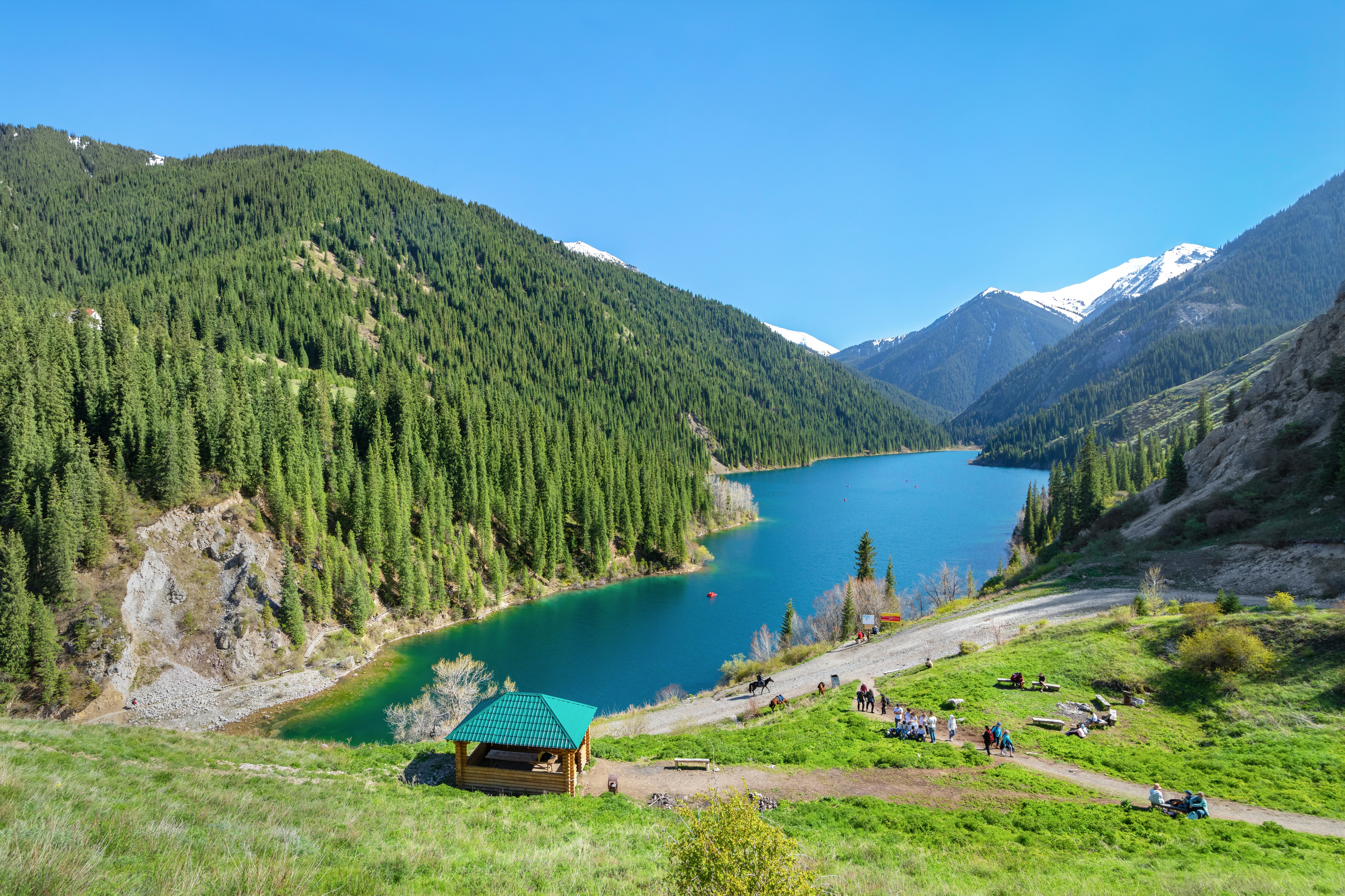 A small hut on the edge of a vast alpine lake surrounded by forest.