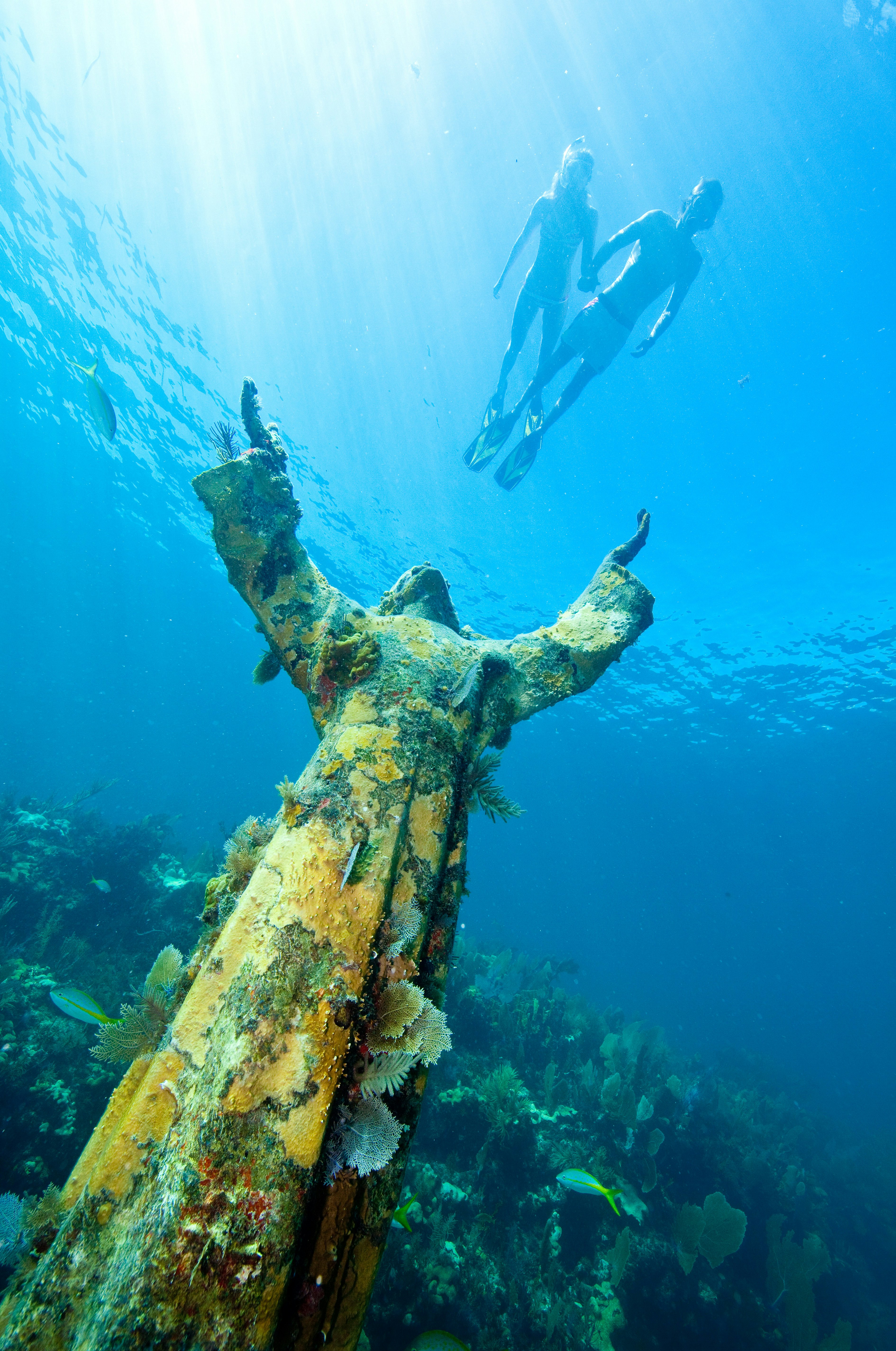 Two people snorkel above a bronze underwater sculpture of Jesus Christ lifting his arms
