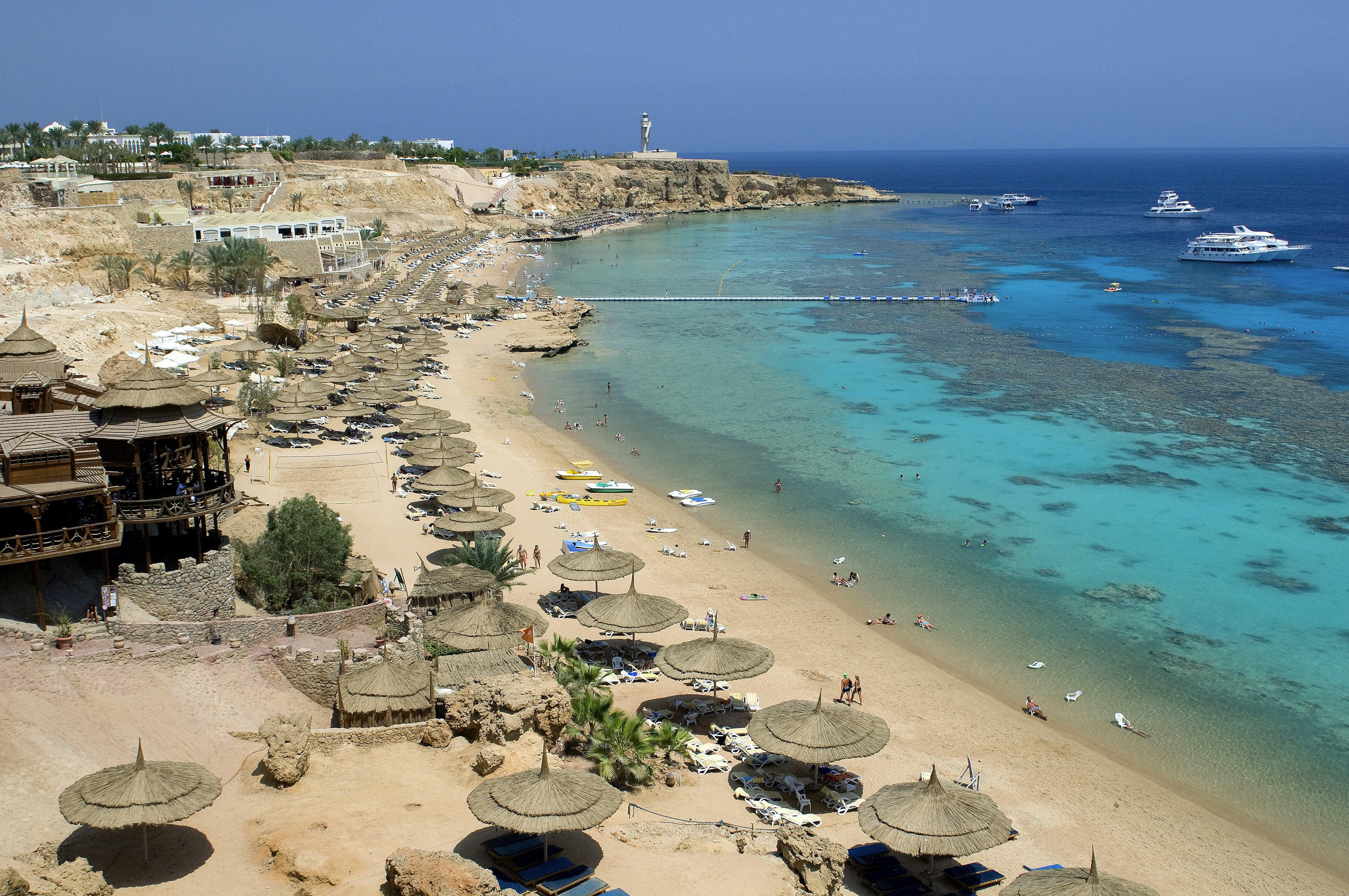 A beach lined with sun shades. Snorkelers swim in the shallows.