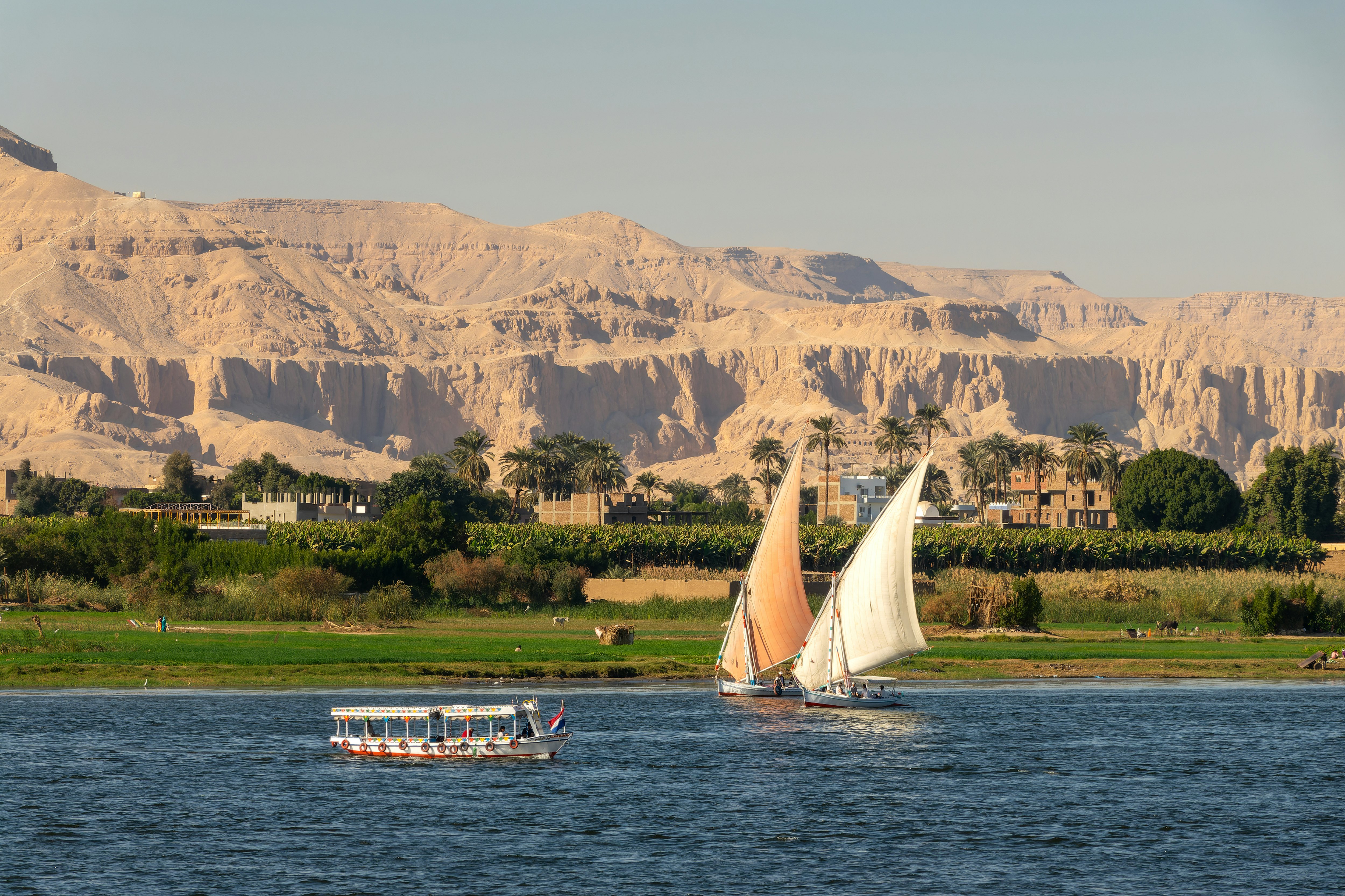 Two sailboats with another boat on a lake with green trees and mountains in the background round
