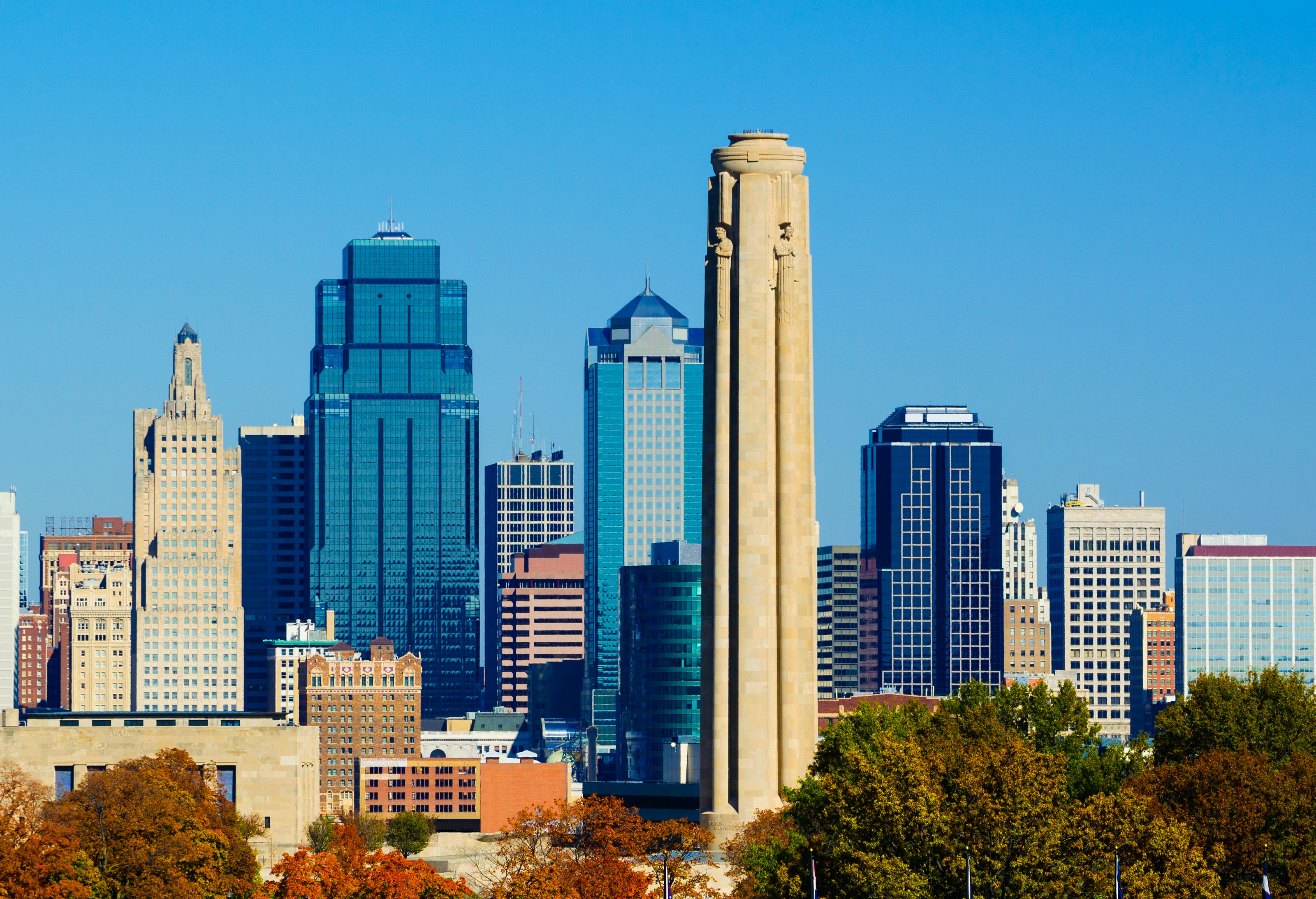 The Downtown Kansas City skyline in the background and the Liberty Memorial monument and Autumn trees in the foreground.