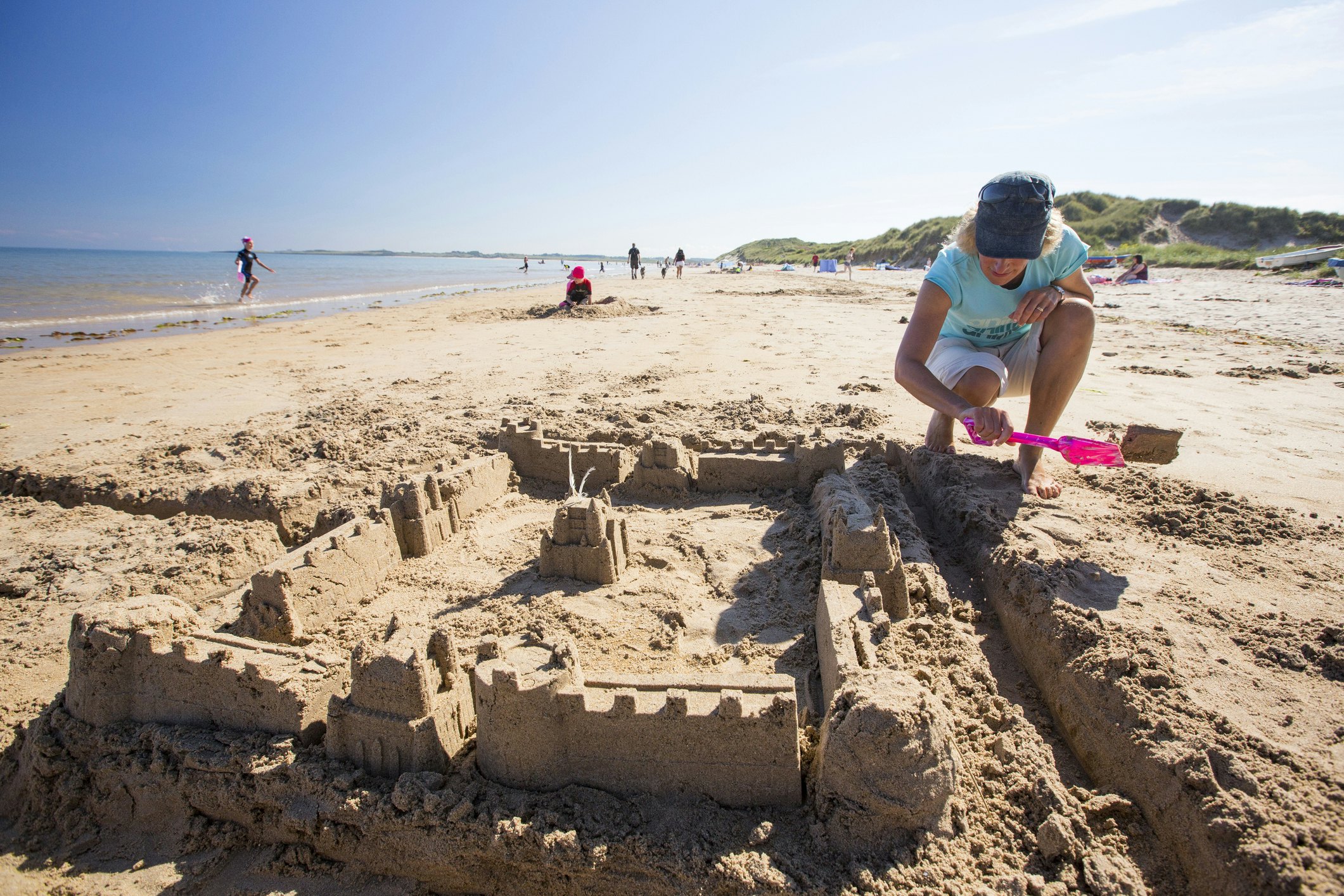 A woman building a sandcastle on Bamburgh Beach, Northumberland, UK.