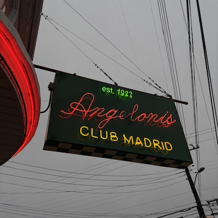 A sign for Angeloni's Club Madrid with green, red and yellow neon letters on a black background