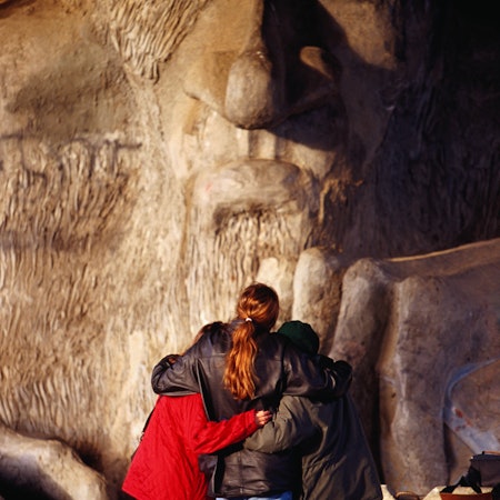 Three people facing a troll sculpture under a bridge in Seattle, Washington.