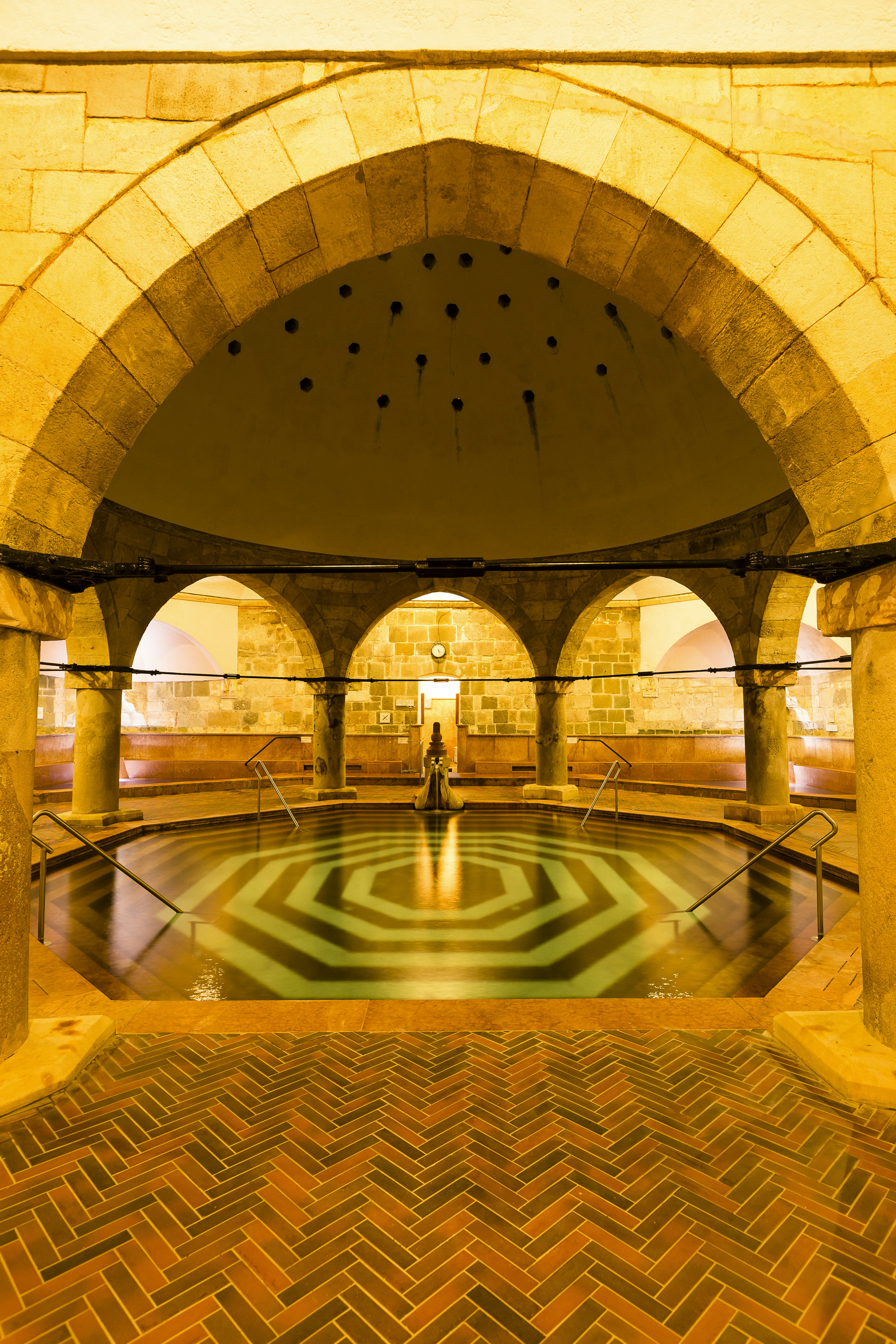 A low-lit room with a central hexagonal pool covered with a dome supported by stone columns.