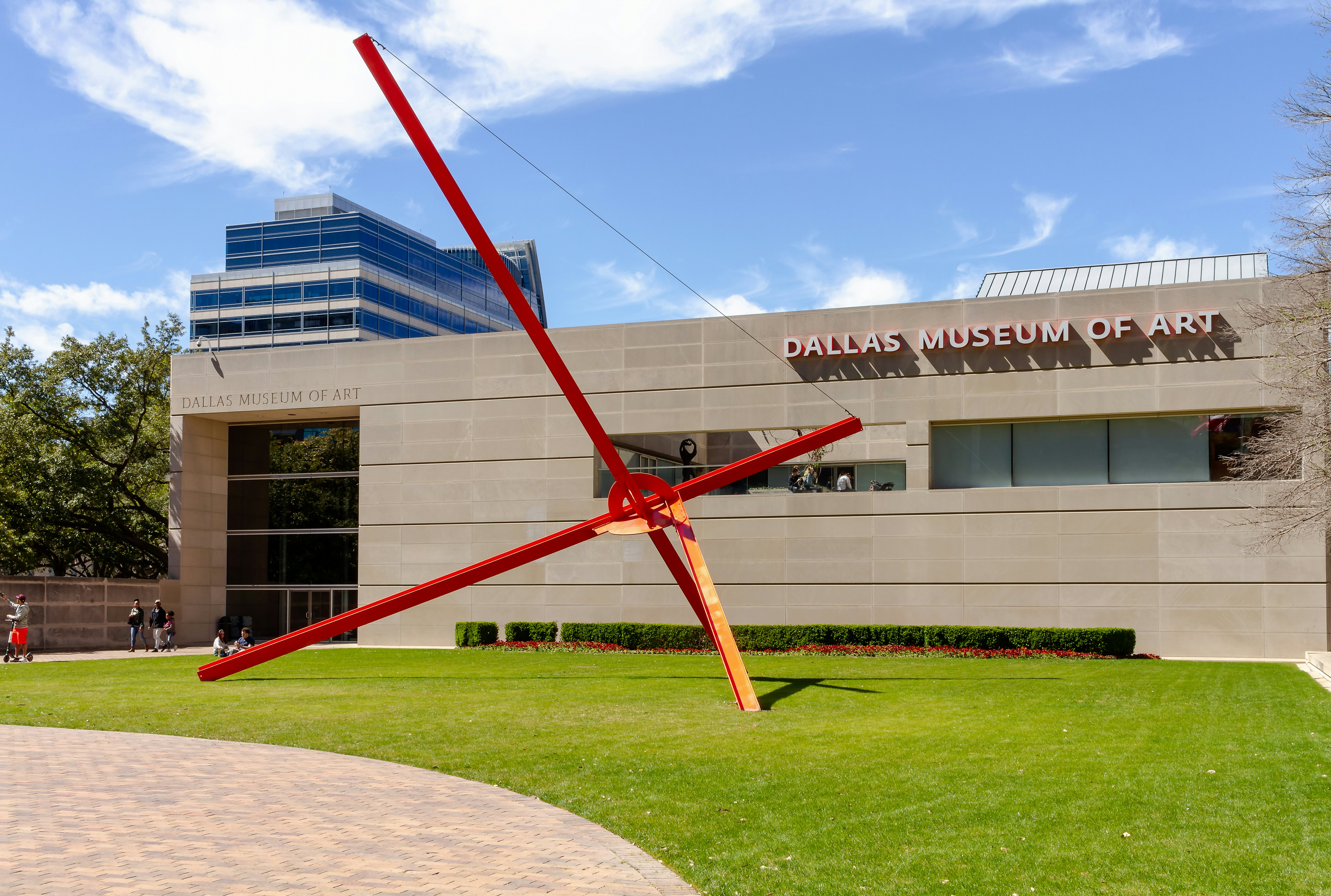 Exterior of a museum building with a large-scale sculpture comprising large red steel bars crossing over with a round intersection.