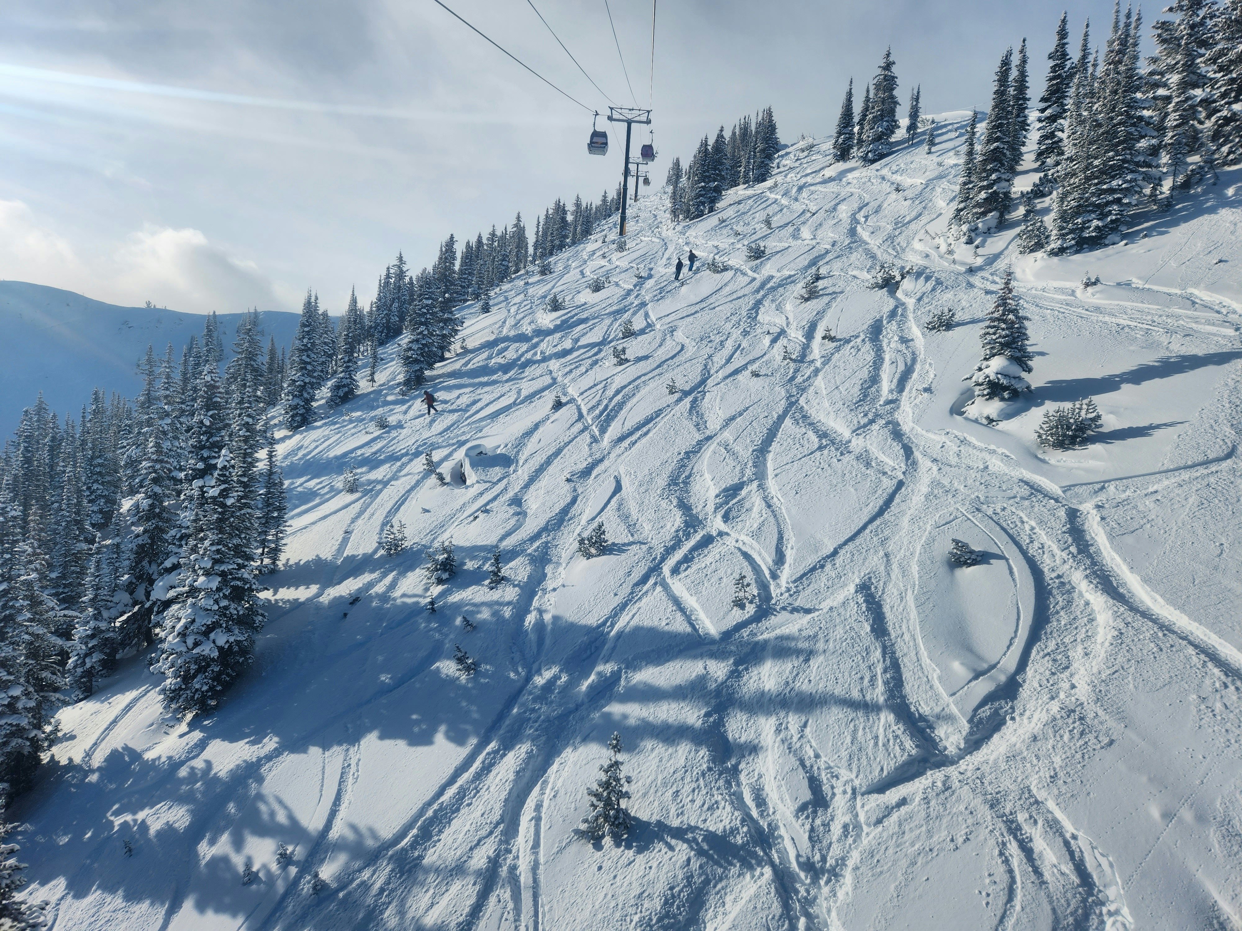 Snowboarders come down a ski slope in a snow-covered resort.