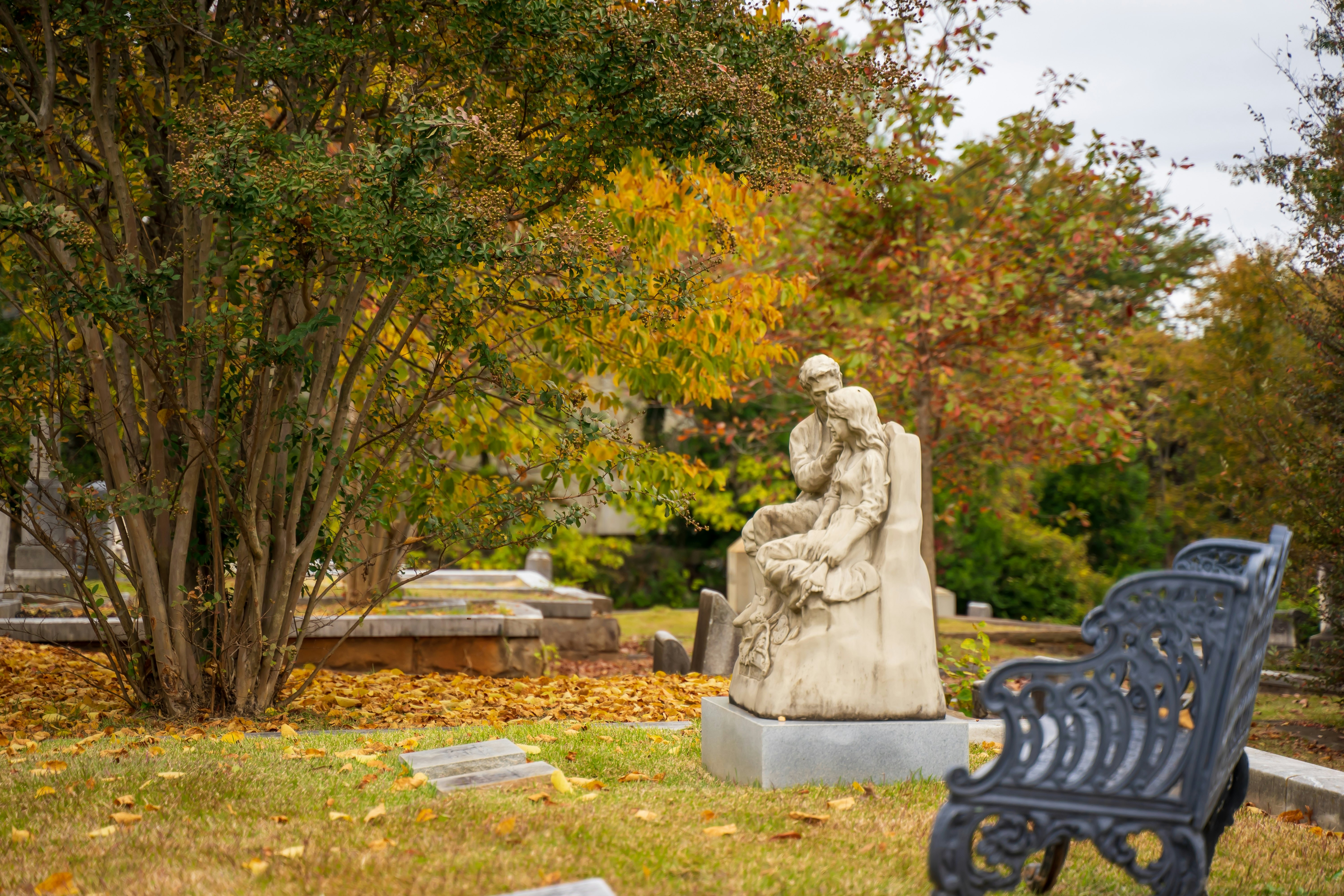Atlanta's Oakland Cemetery in the fall, with a nearby bench and a statue of a man moving a lock of hair off a woman's face