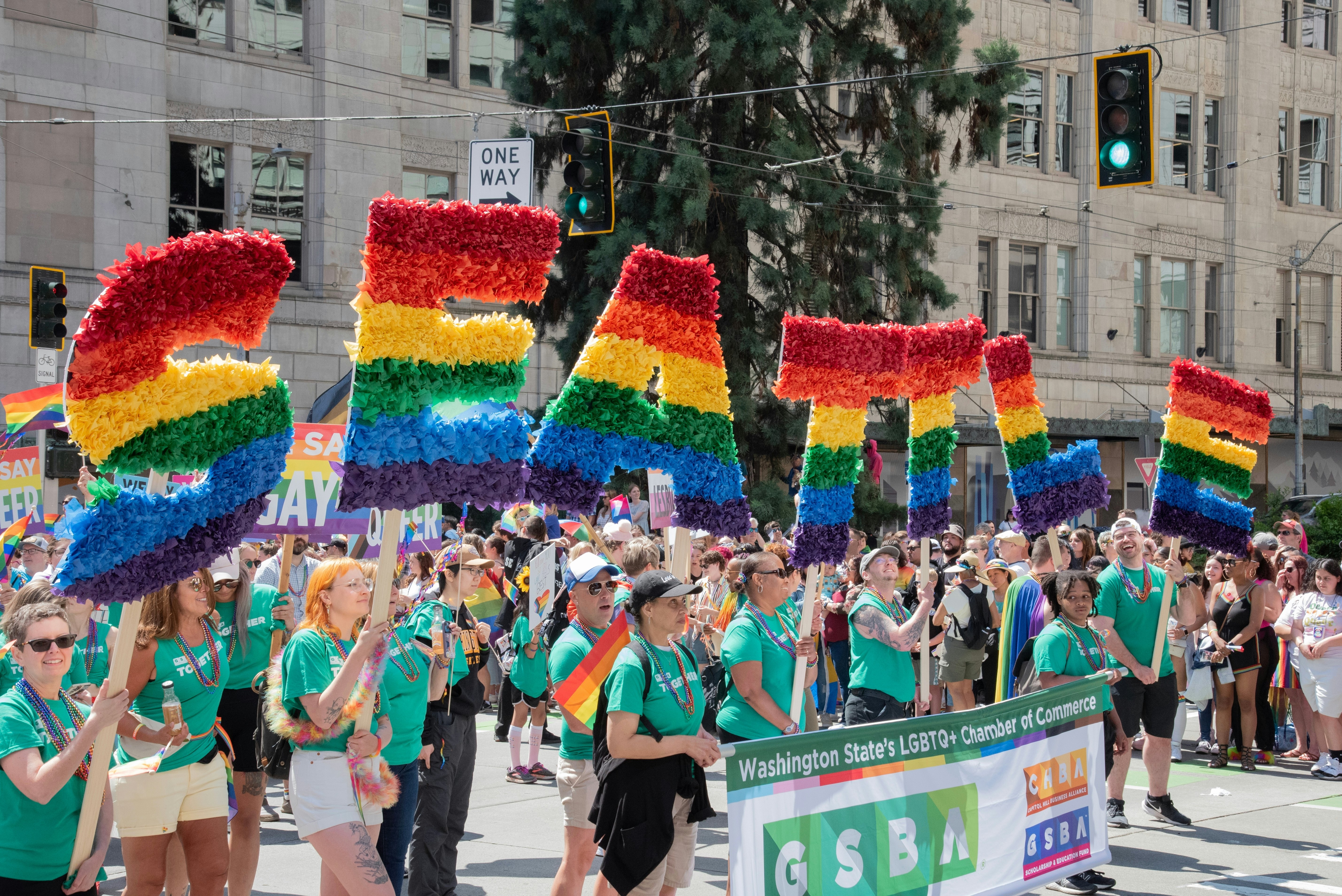 Pride parade with SEATTLE spelled out in rainbow colors with many smiling diverse people