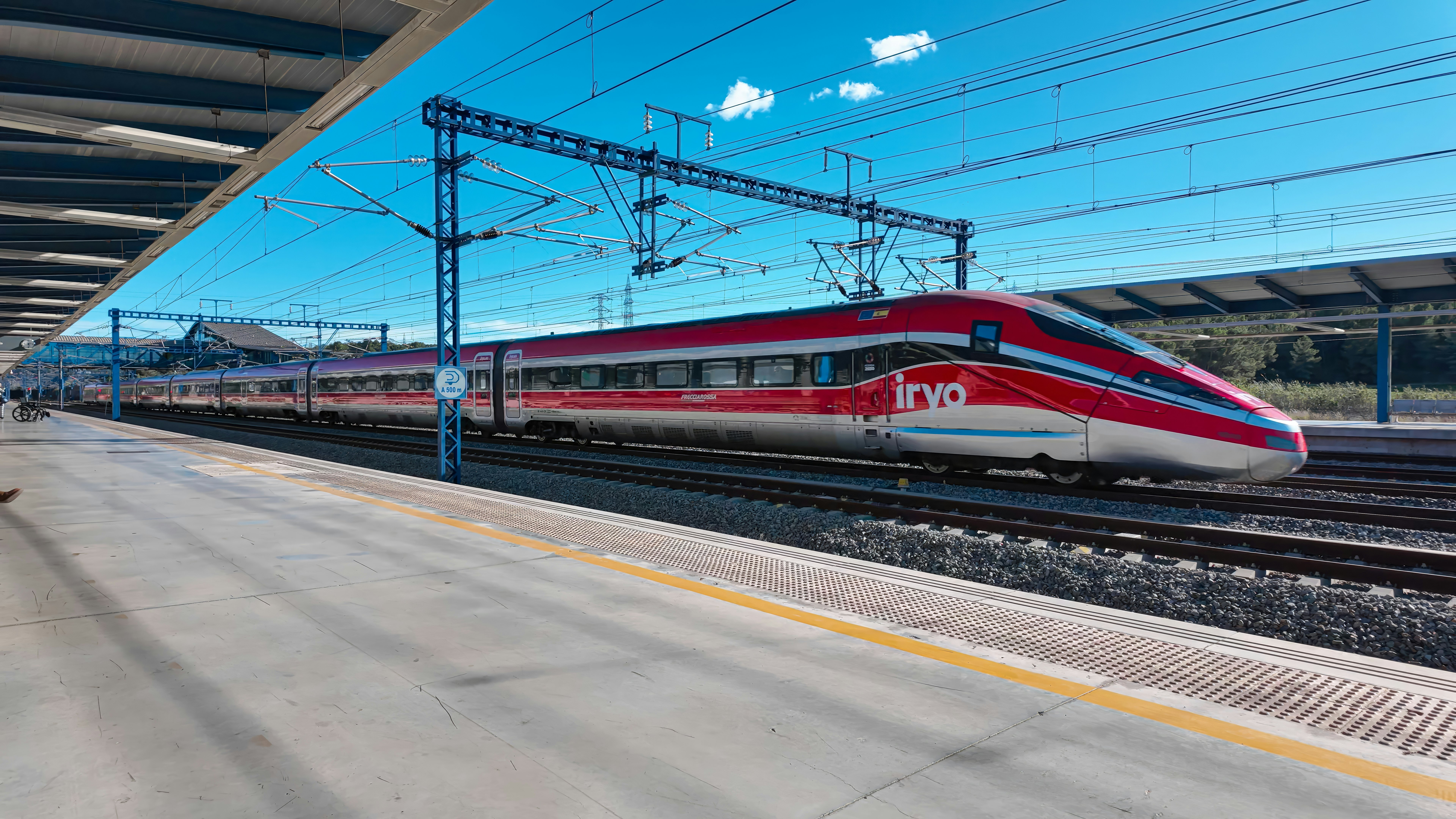 A high-speed red train running on tracks through a station.