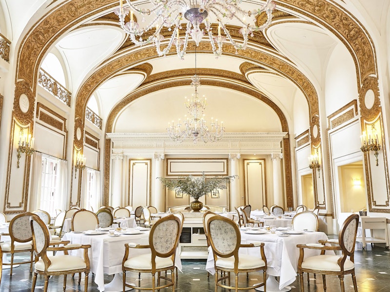 Ornate dining room with curved ceilings and upscale white and gold walls, tables, and chairs.