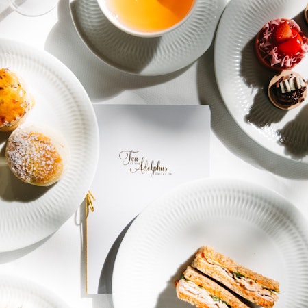 Close-up of cakes on plates and a menu reading "Tea at the Adophus."