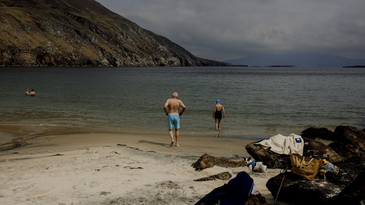 Bathers walk into a beach surrounded by a steep hill