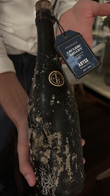 A hand holding a dark bottle of champagne labeled "Leclerc Briant"