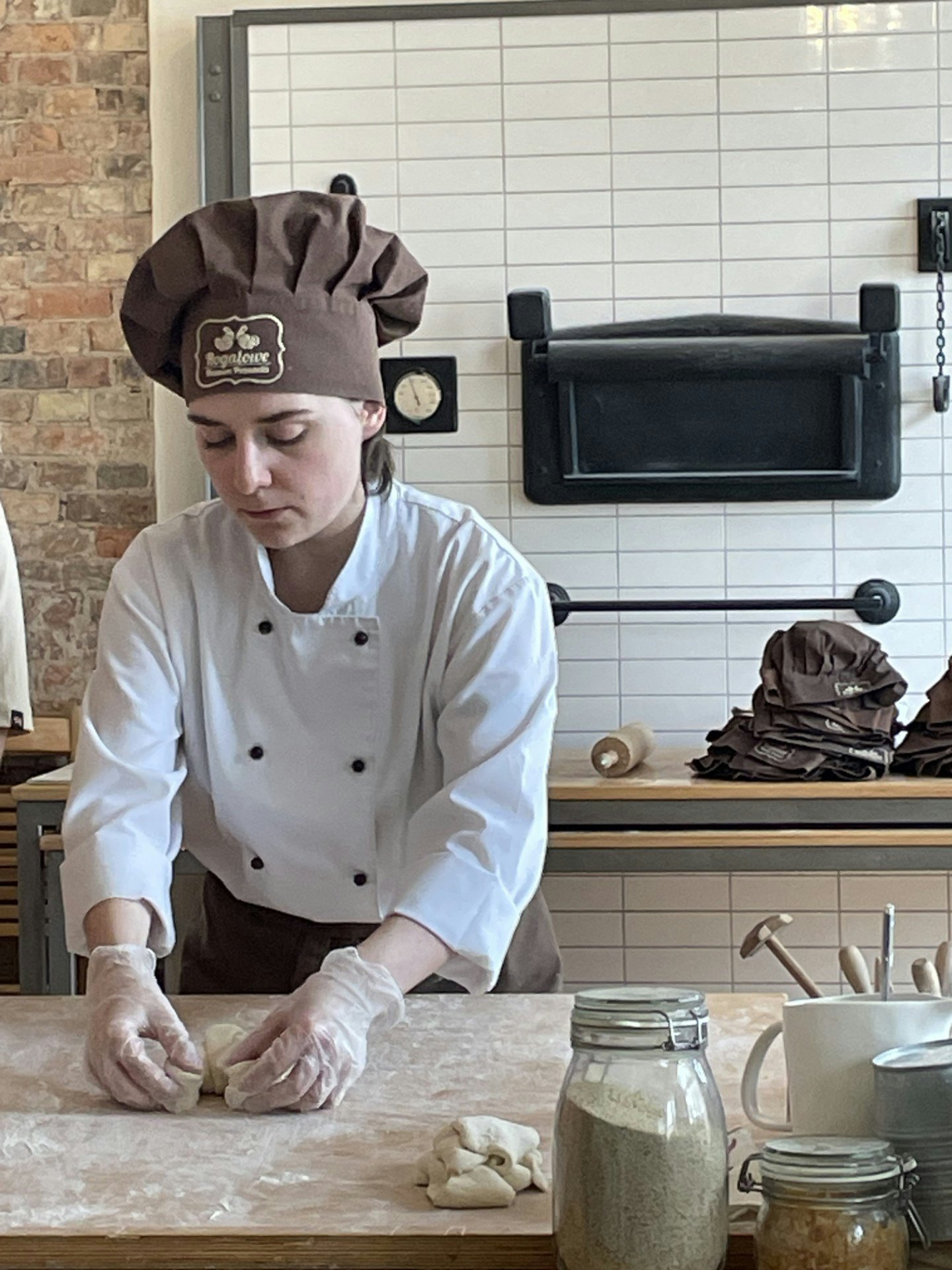 A woman in a chef's uniform and gloves rolls dough into a croissant on a floured table