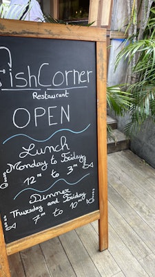 A chalkboard placard for Fish Corner restaurant with its hours on it