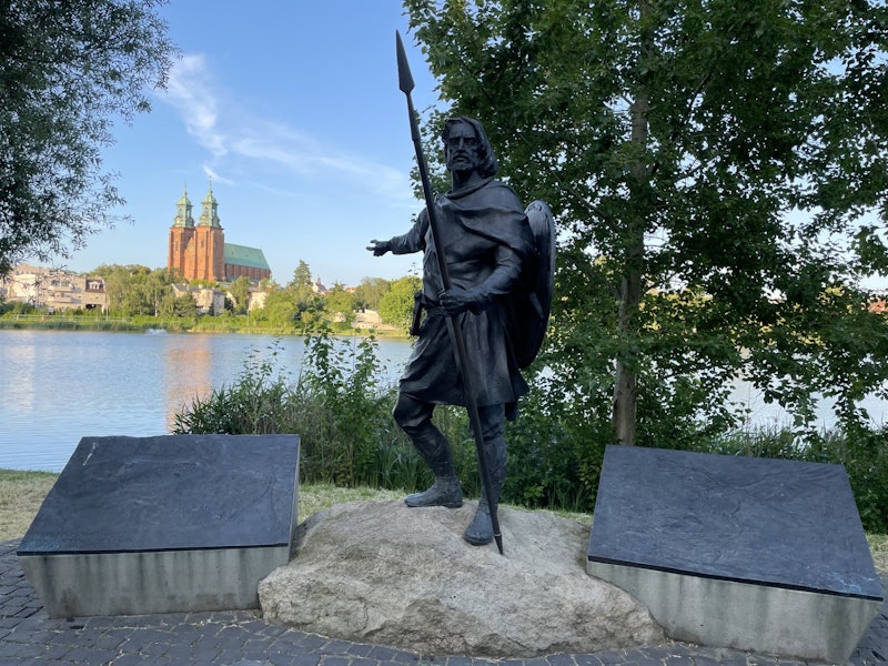 Statue of a man with a spear with a body of water and buildings behind it